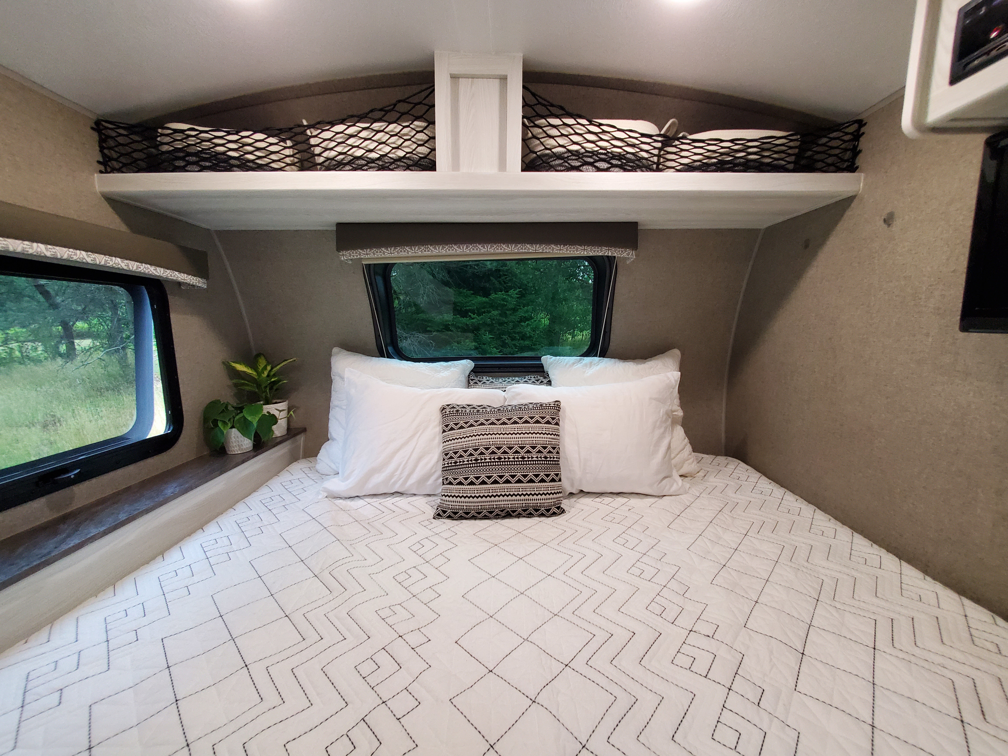 Comfortable RV rental bedroom featuring a bed with white bedding, overhead mesh storage, and a window.. Forest River Rockwood Geo Pro 2019