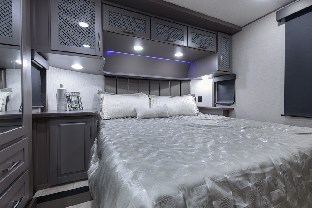Luxury RV rental bedroom showcasing a large bed, modern cabinets, and ambient lighting for ultimate comfort.. Grand Design Momentum 2022