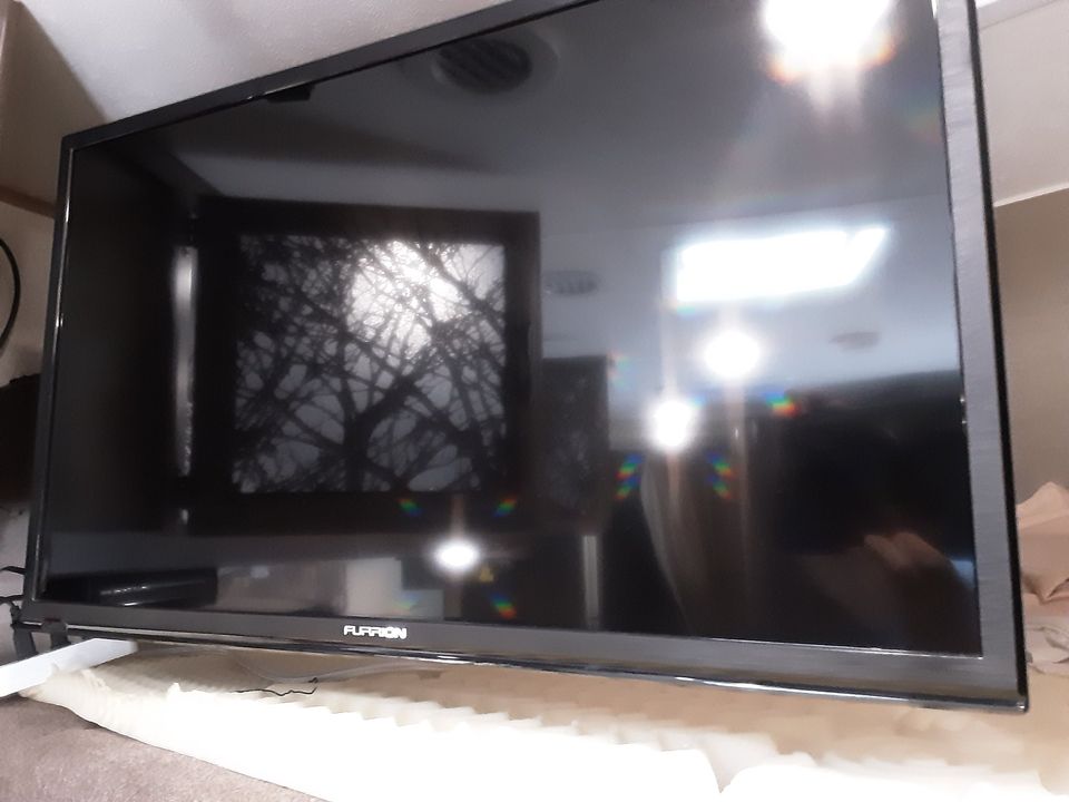 A Furrion TV in an RV rental. Its reflective screen shows interior lights & silhouetted trees outside.. Forest River Coachmen Freelander 2018