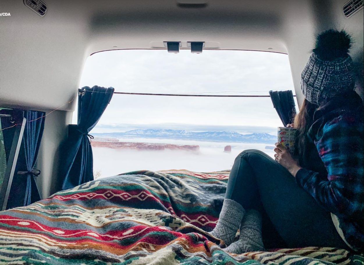 From an RV rental, a traveler sips coffee, enjoying foggy mesas and distant mountains from a cozy van bed.. Ford transit 2022