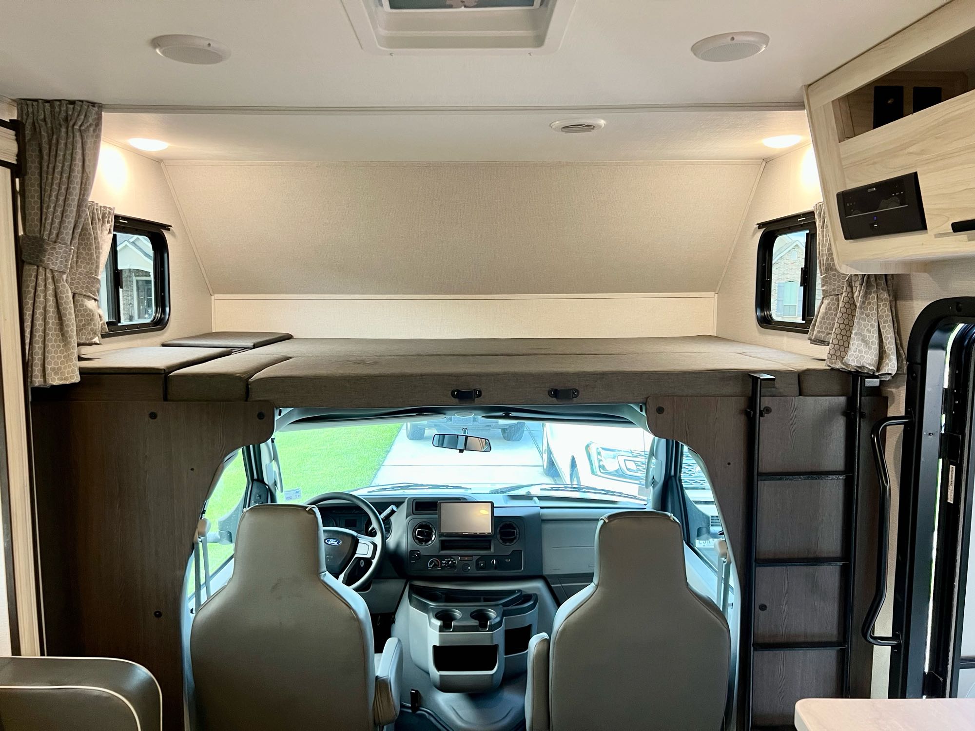 The interior of an RV rental: a cozy over-cab bunk overlooks the driver's cab and dashboard.. Forest River Sunseeker Classic 2021