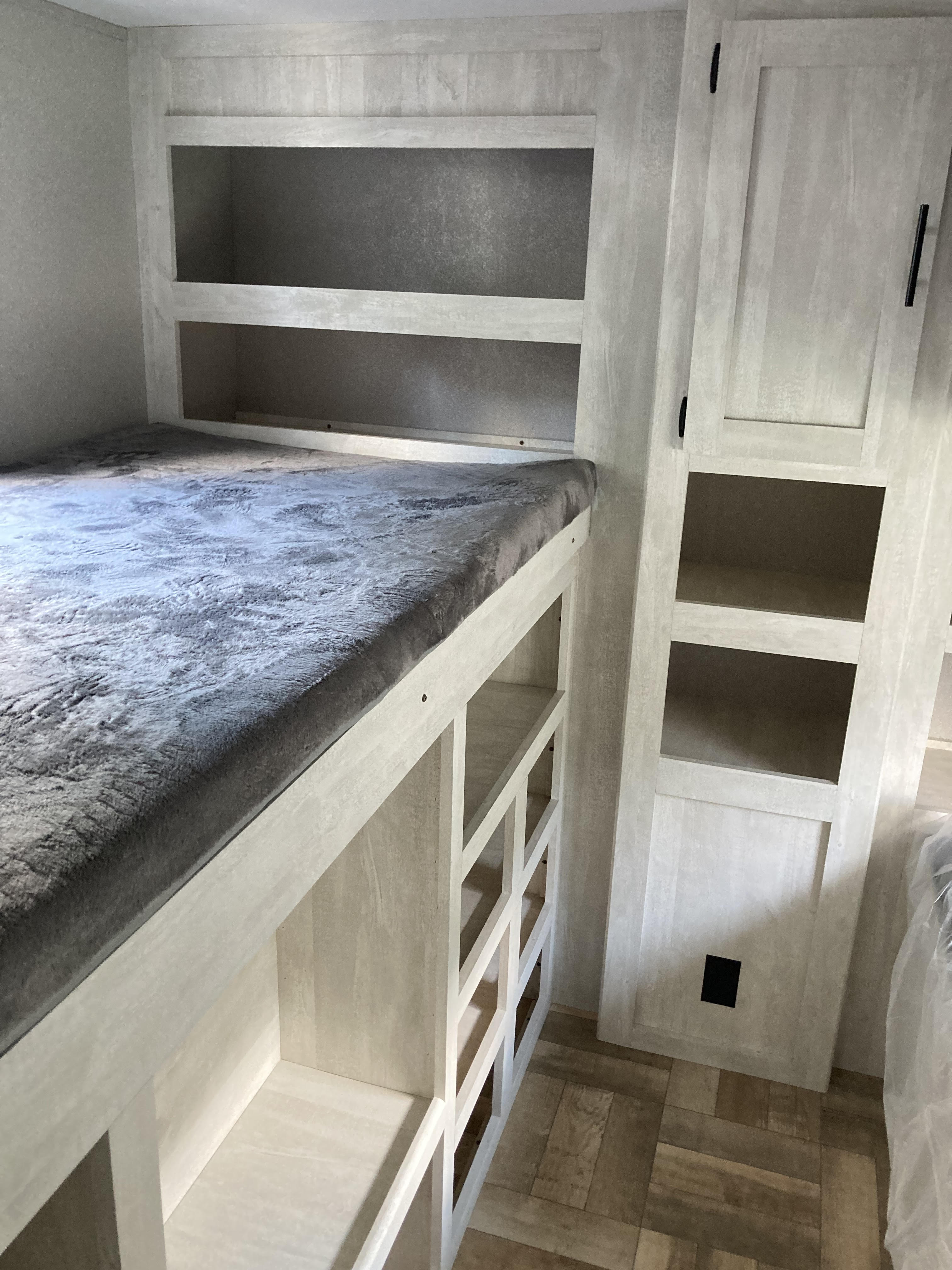 RV rental interior featuring a modern bunk bed with open storage shelves, a tall cabinet, and light wood finishes.. Shasta RV 310K 2022