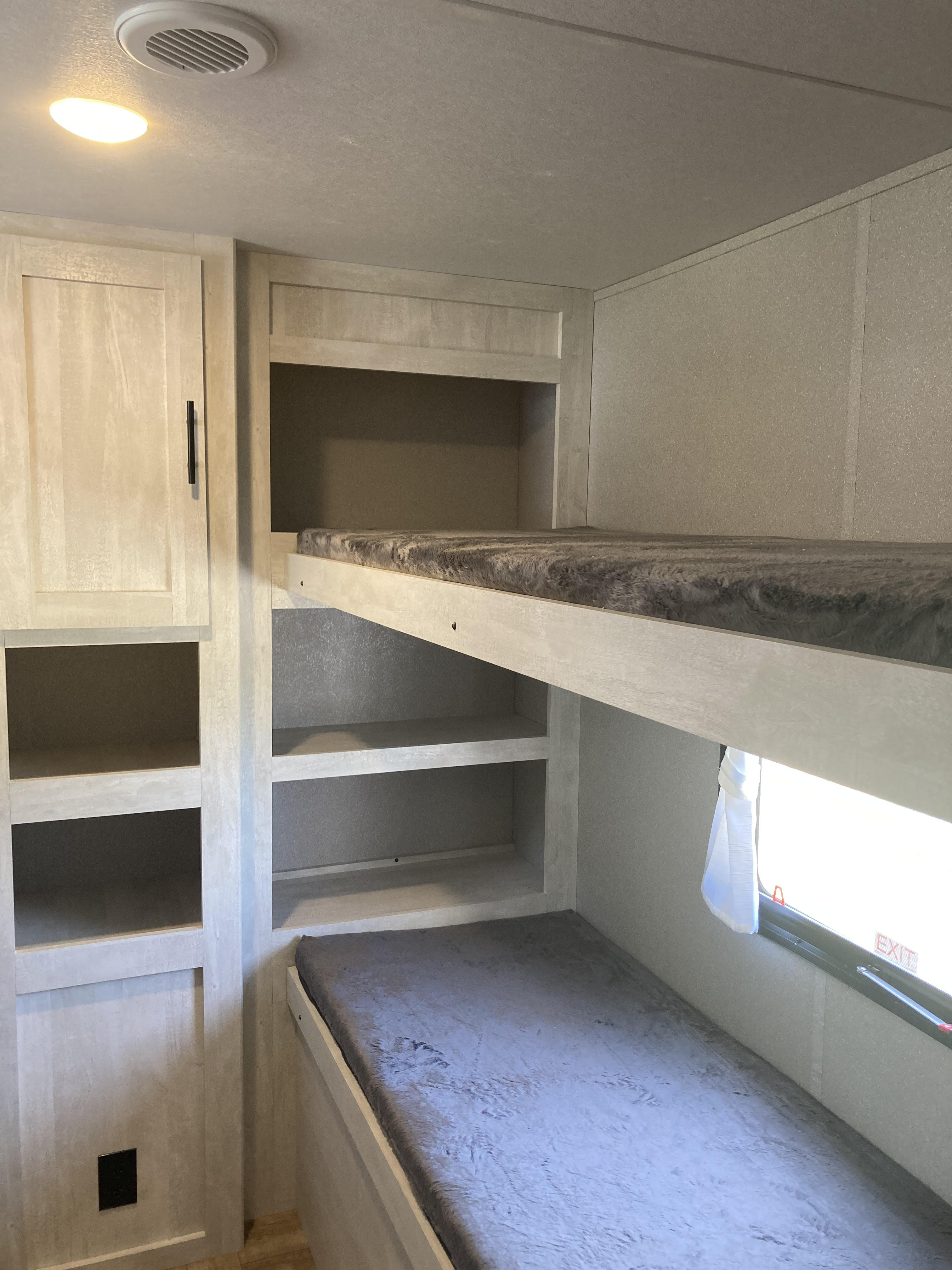 Cozy RV rental bunk beds with built-in storage shelves, light-colored walls, and a window for comfortable stays.. Shasta RV 310K 2022