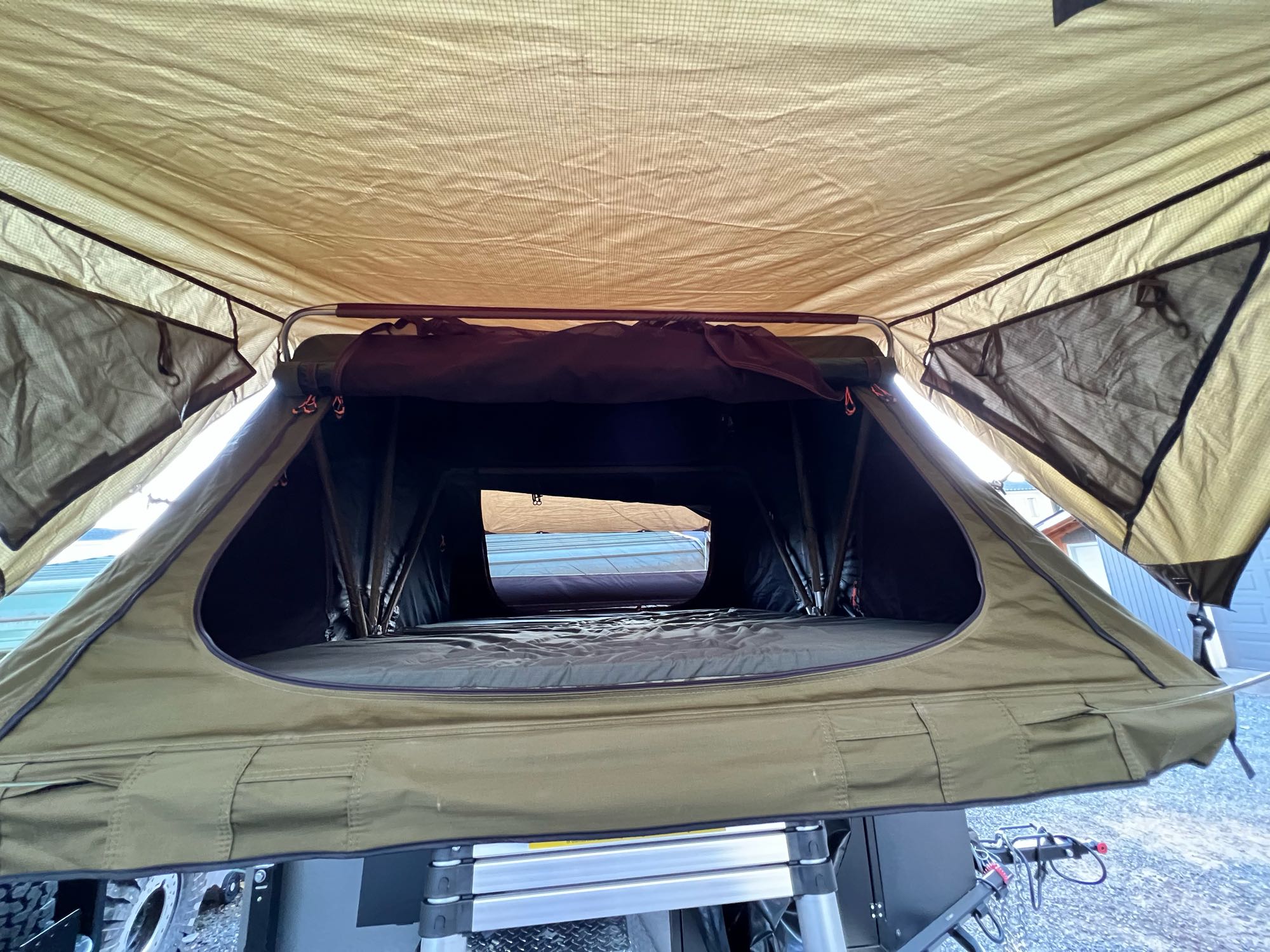 Inside a spacious olive-green rooftop tent, showing the mattress and open windows. Perfect for an RV rental camping adventure.. Vorsheer XER 2022