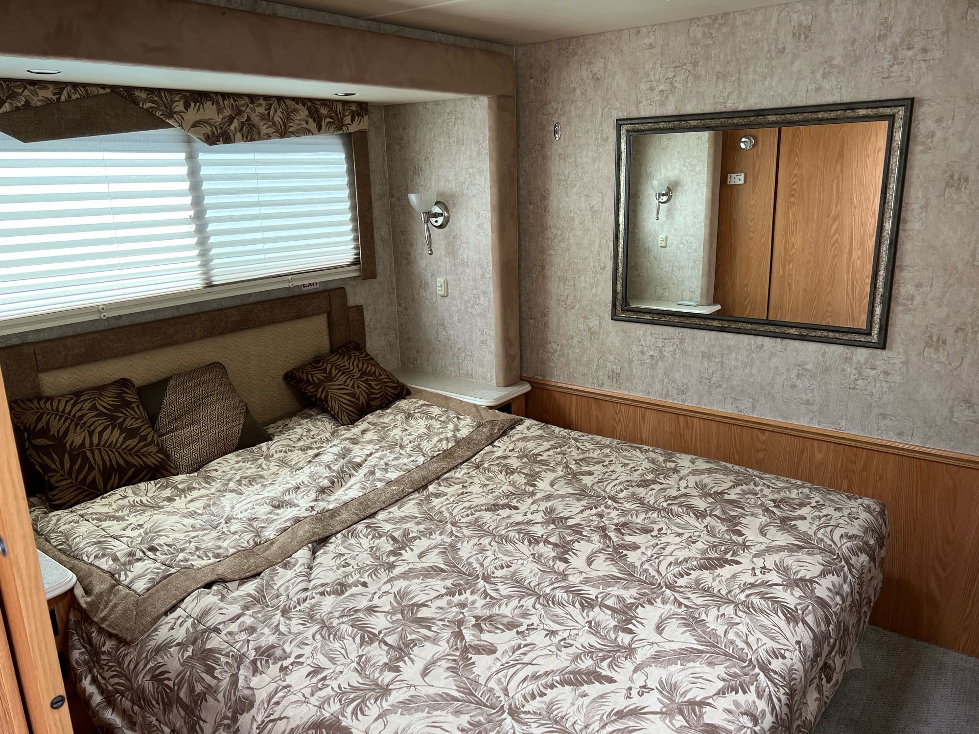 RV rental bedroom view: large bed with nature-patterned bedding, window with blinds, and mirrored wall. Comfortable travel space.. National RV Sea Breeze 2006