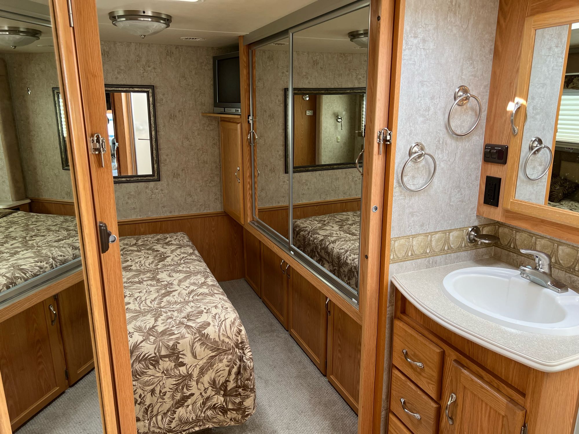 RV rental bedroom and bathroom interior: compact design with a bed, TV, sink, mirrors, and storage solutions.. National RV Sea Breeze 2006