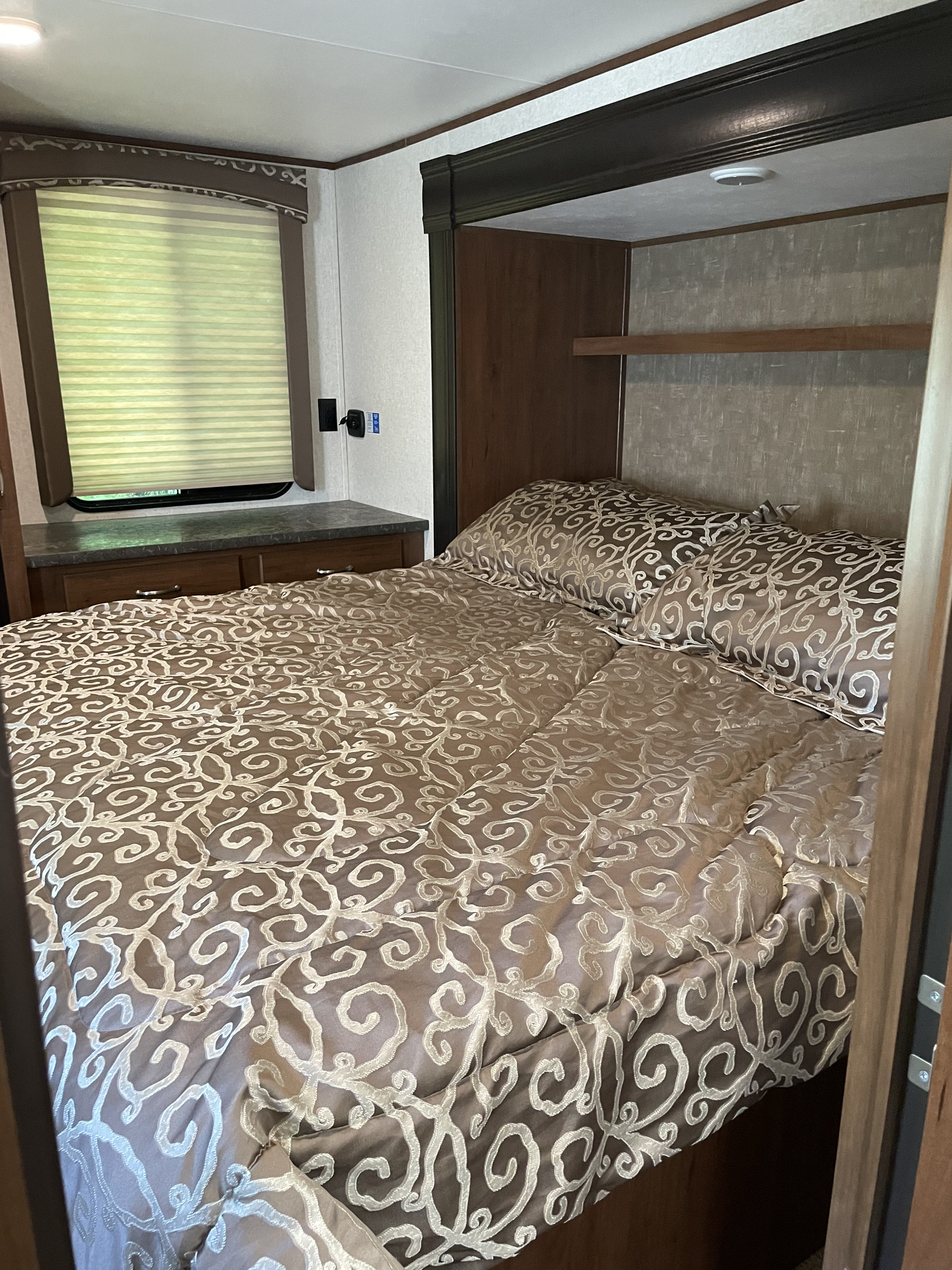 Experience comfort in this RV rental bedroom: brown & white patterned bedding, built-in storage, and window blinds. A cozy sleep space.. Jayco Jay Flight 2018