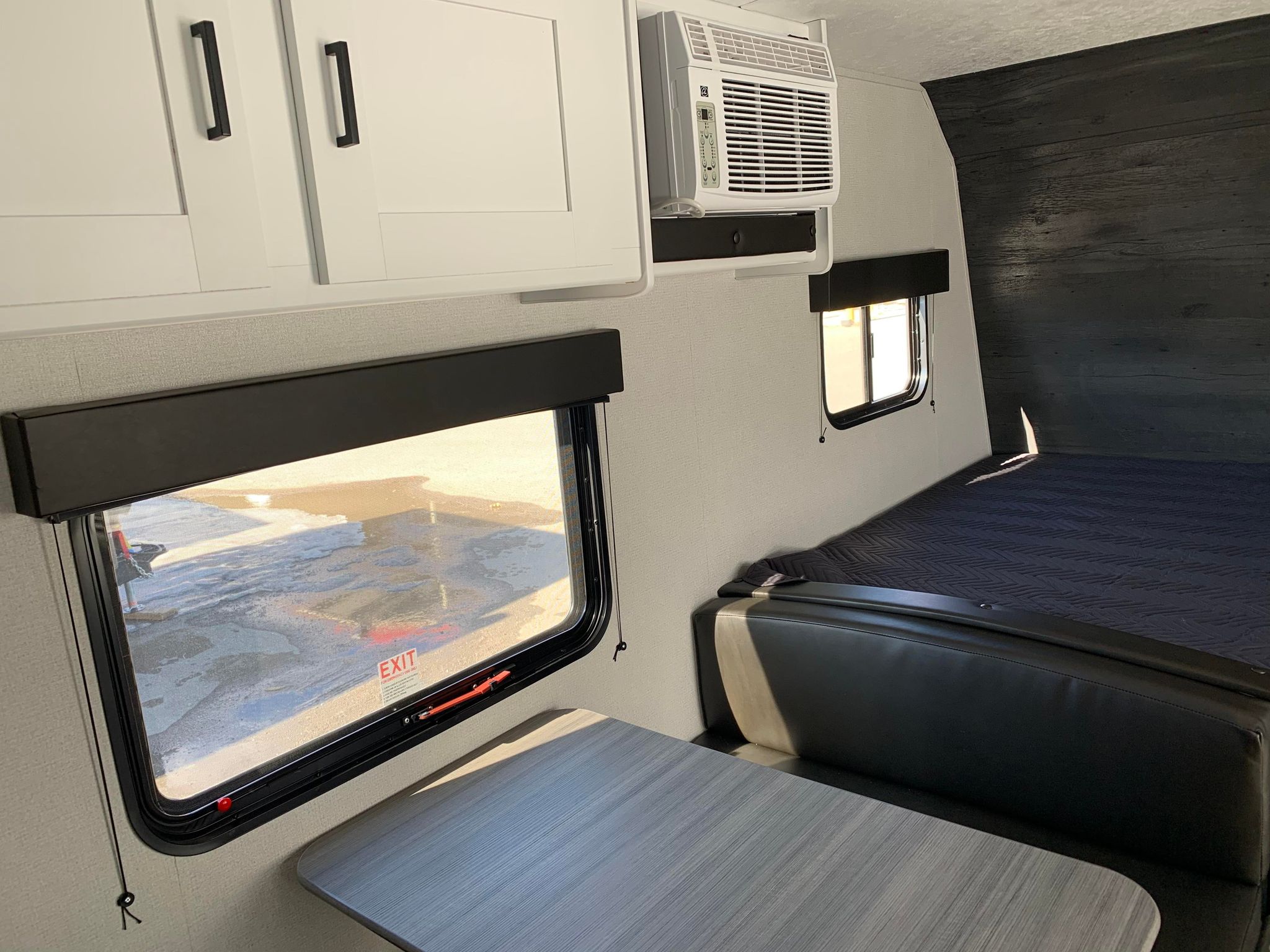 This RV rental features bright white cabinets, a wall AC unit, dining booth, and bed in a modern, functional space.. Keystone RV Hideout 2021