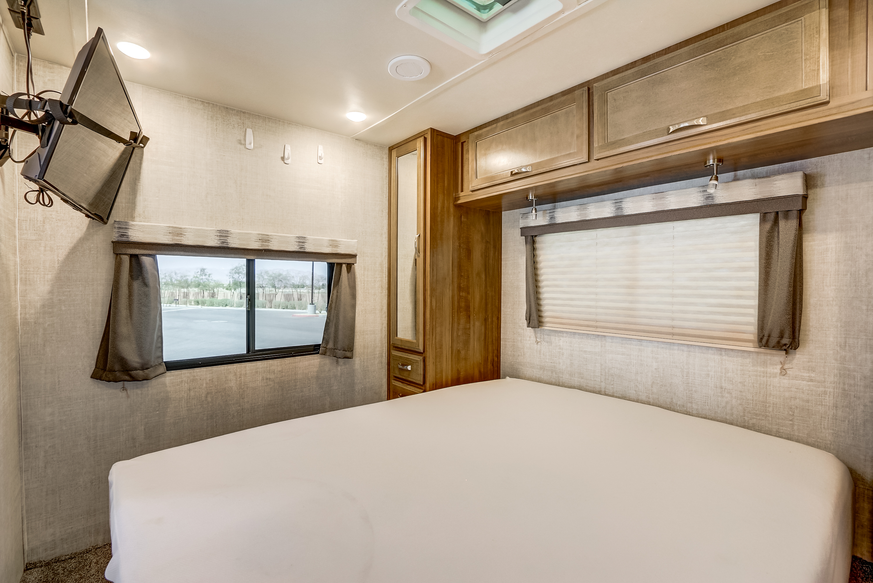 Cozy RV rental bedroom features a comfy bed, wall-mounted TV, storage cabinets, and window.. Gulf Stream Conquest 2020