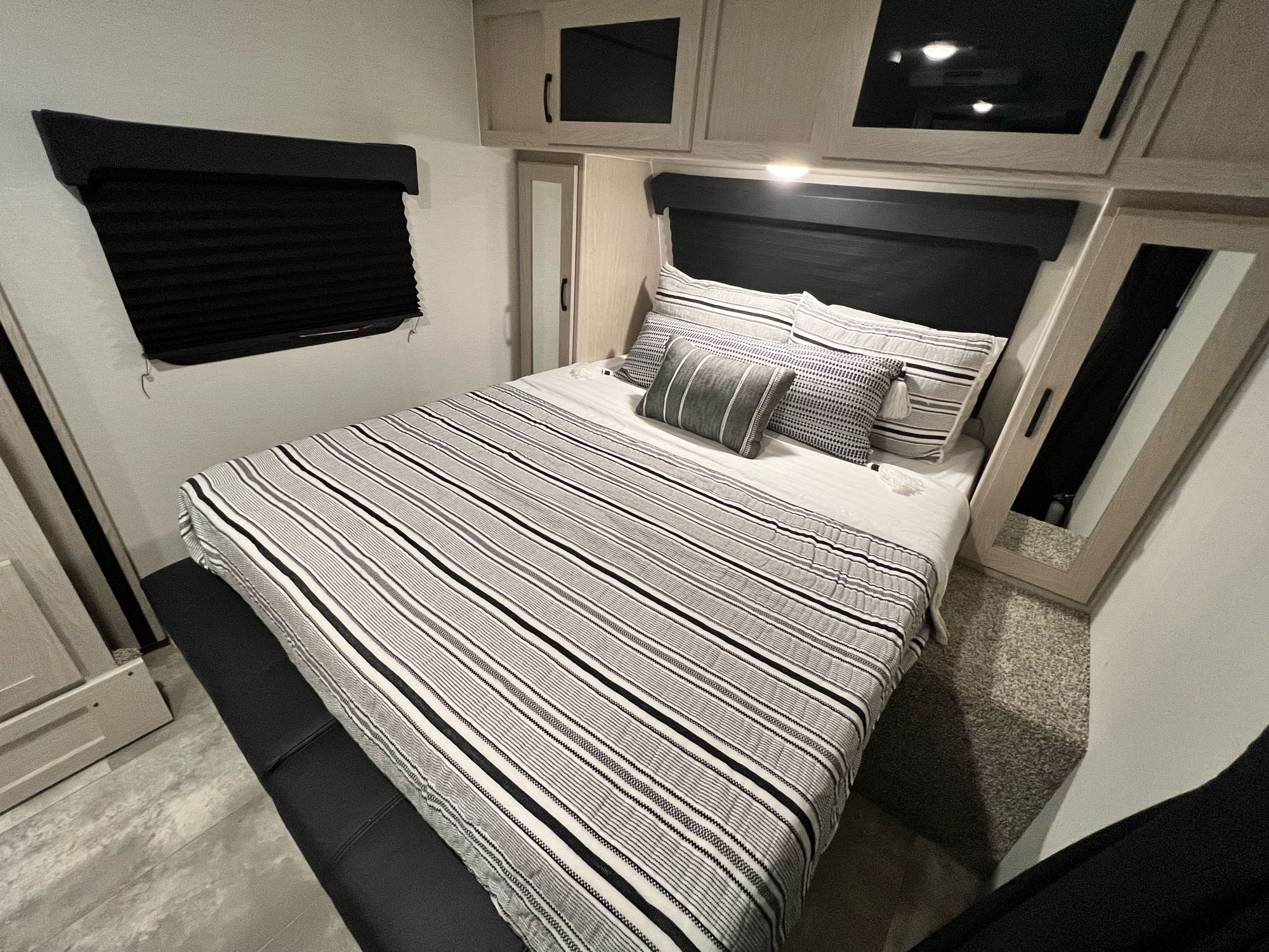 Discover this RV rental bedroom: queen bed with striped bedding, black window blind, overhead cabinets, and floor seating.. Coachmen Apex Nano 2022
