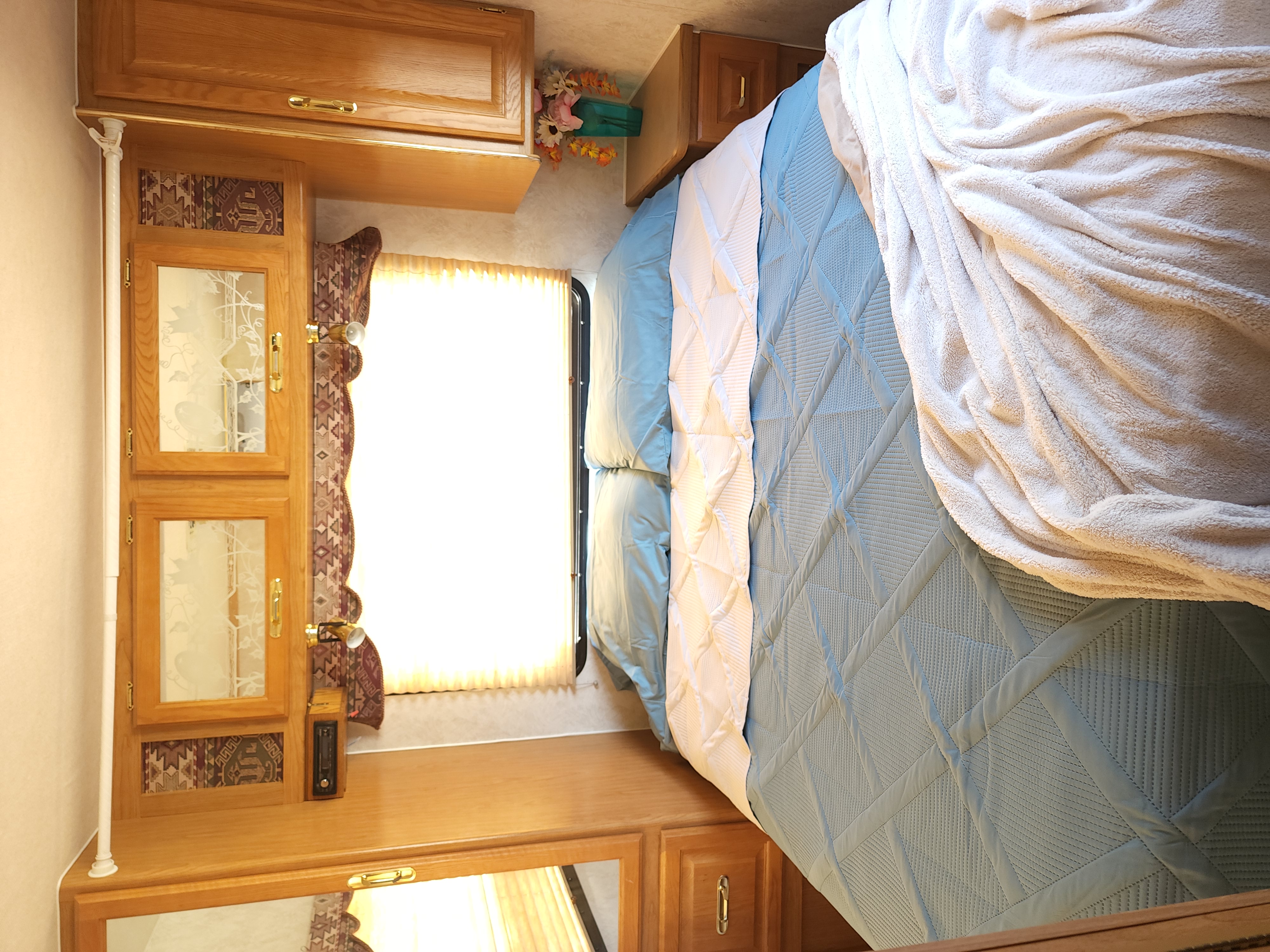 Relaxing RV rental bedroom: light blue quilted bed, detailed wood cabinetry, and bright window. Your comfortable travel home.. Triple E Senator 1998
