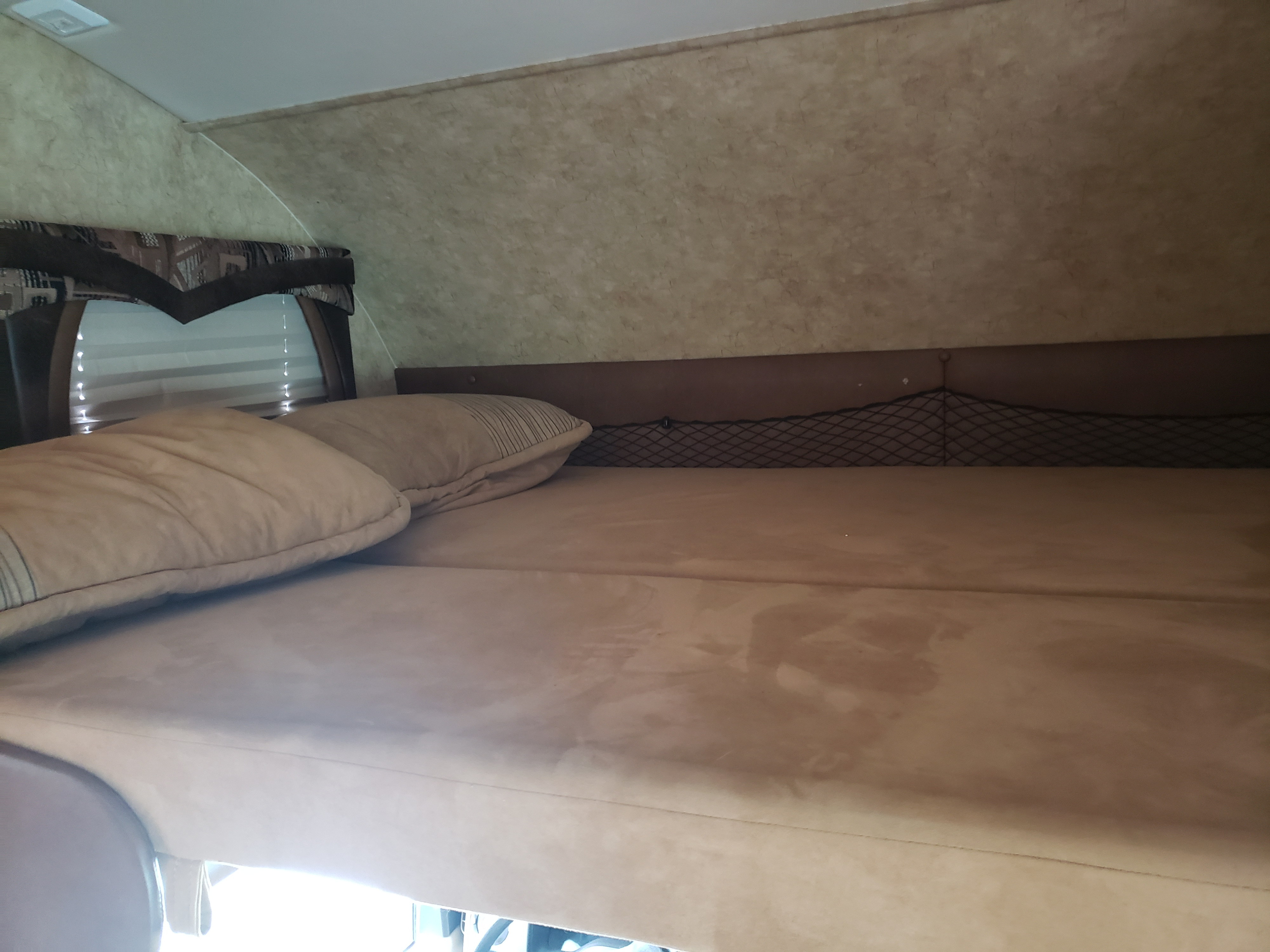 Cozy rv rental sleeping area with a comfortable bed, pillows, window blinds, and a handy storage net.. Jayco Greyhawk 2011