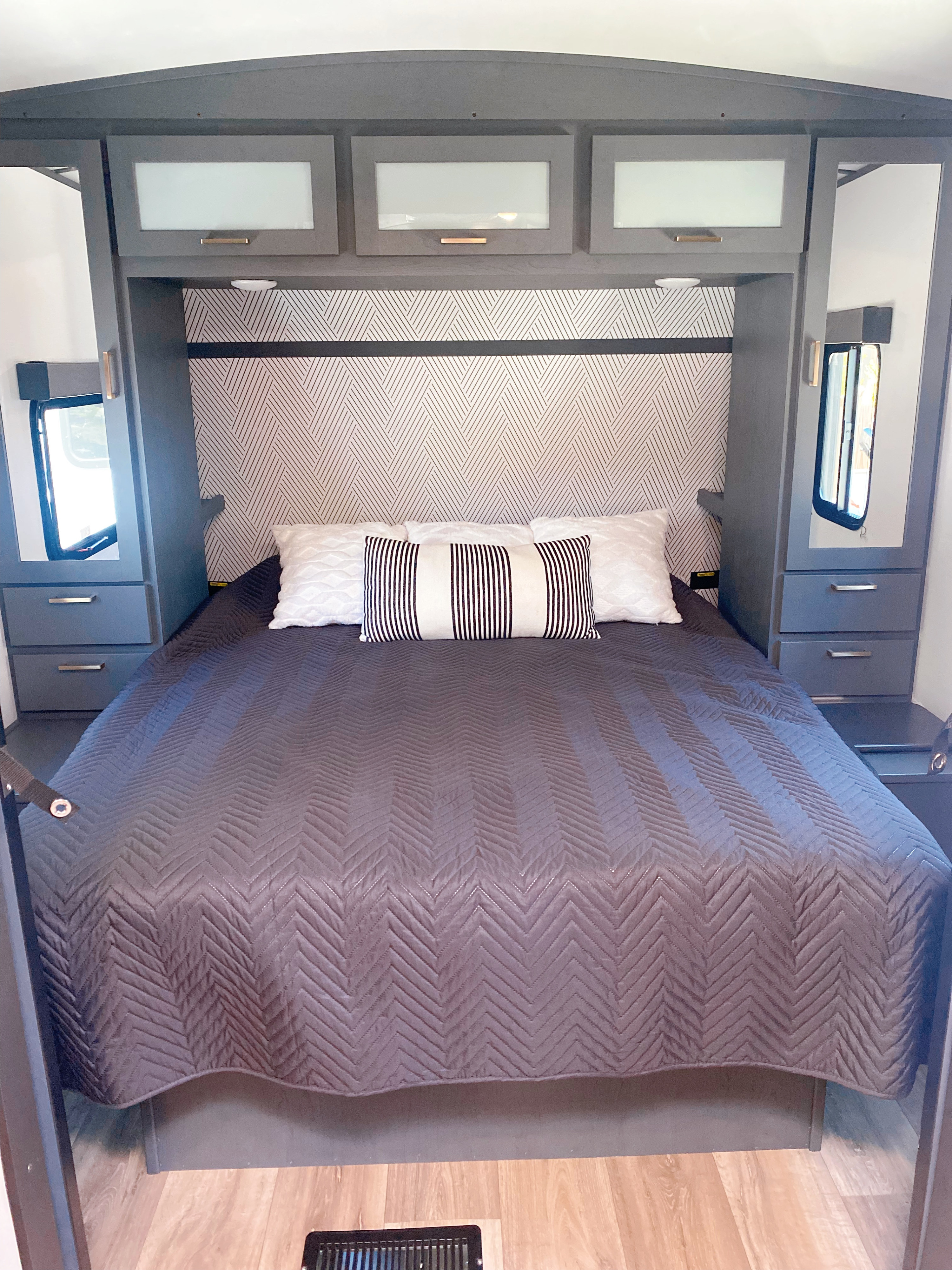 Modern RV rental bedroom with dark gray quilted bed, geometric wallpaper, and smart storage.. Keystone RV Bullet Ultra Lite 2022