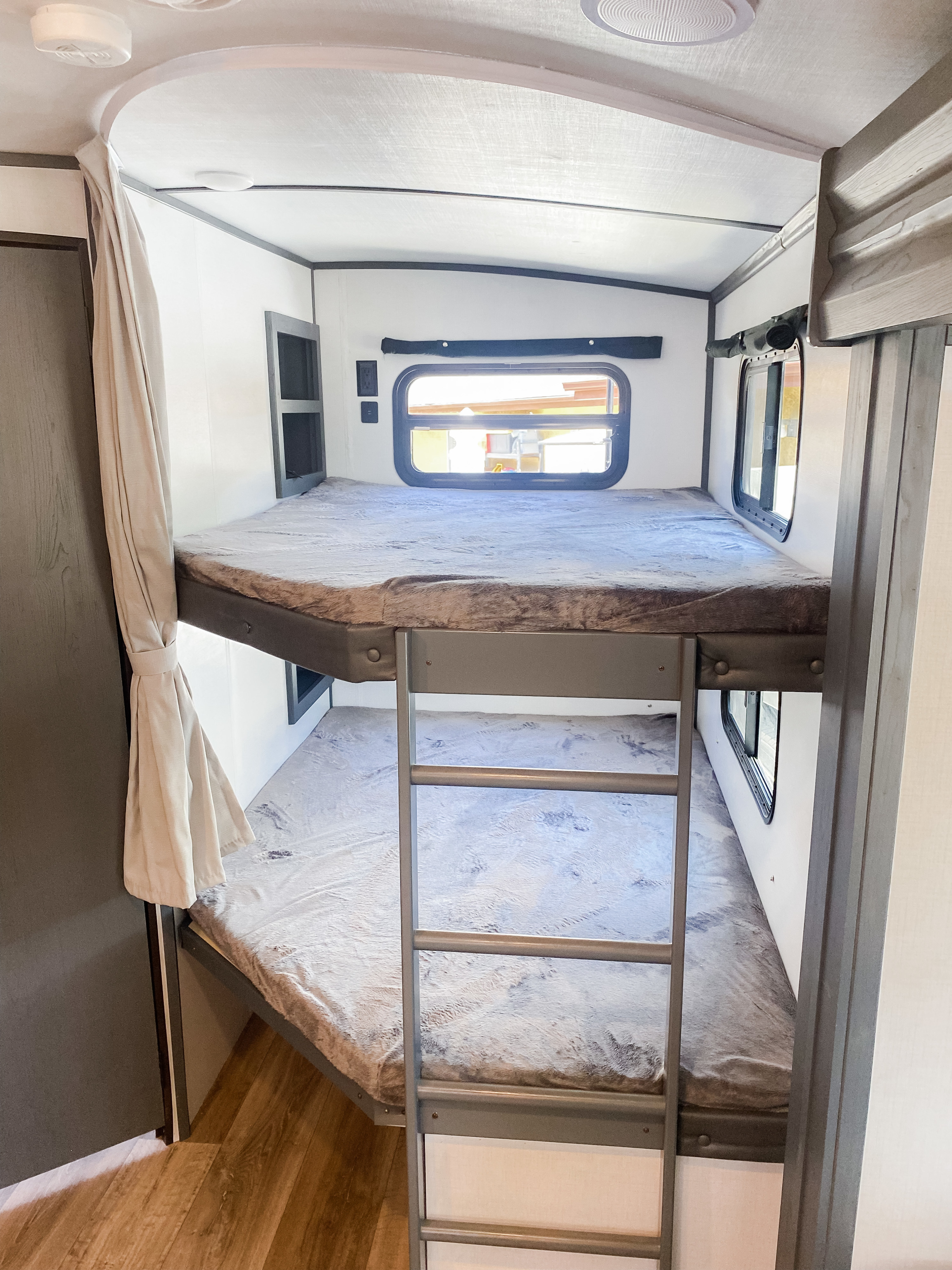 Cozy bunk beds in an RV rental, featuring fluffy grey bedding, a window, and an access ladder, perfect for family adventures.. Keystone RV Bullet Ultra Lite 2022
