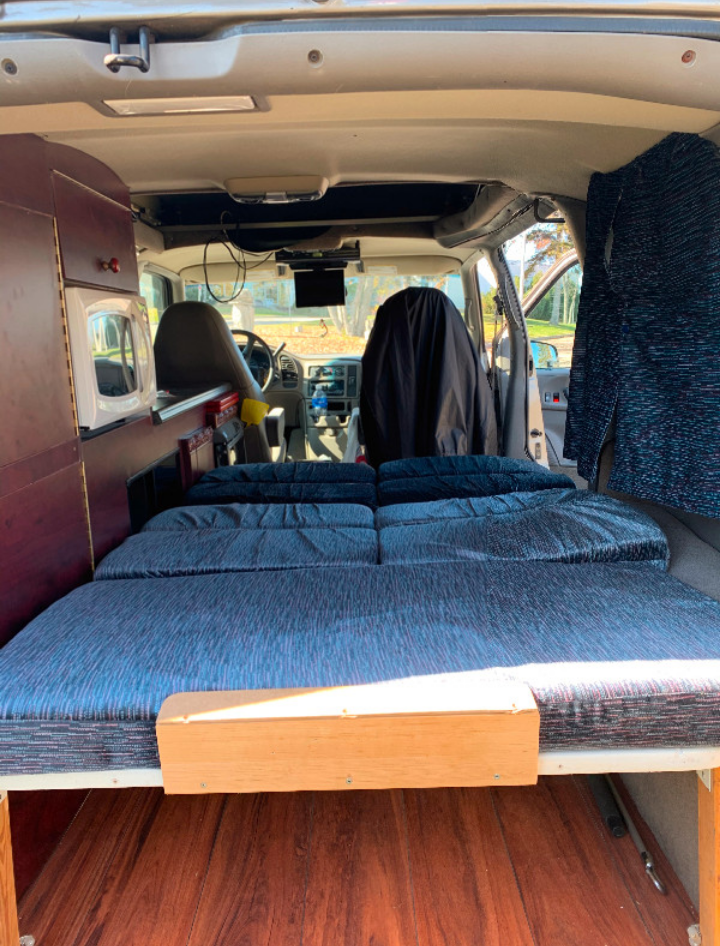 This RV rental features a camper van's interior: a comfortable bed, compact kitchen with microwave, and front cabin views.. Chevrolet Safari Condo 2002