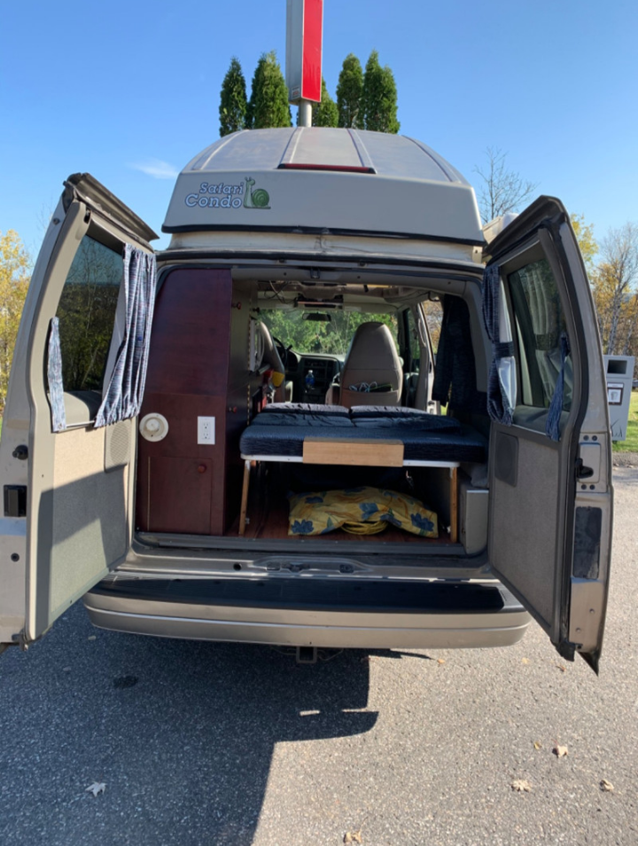 Explore this compact RV rental: a Safari Condo camper van with its rear doors open, revealing a bed & custom interior.. Chevrolet Safari Condo 2002