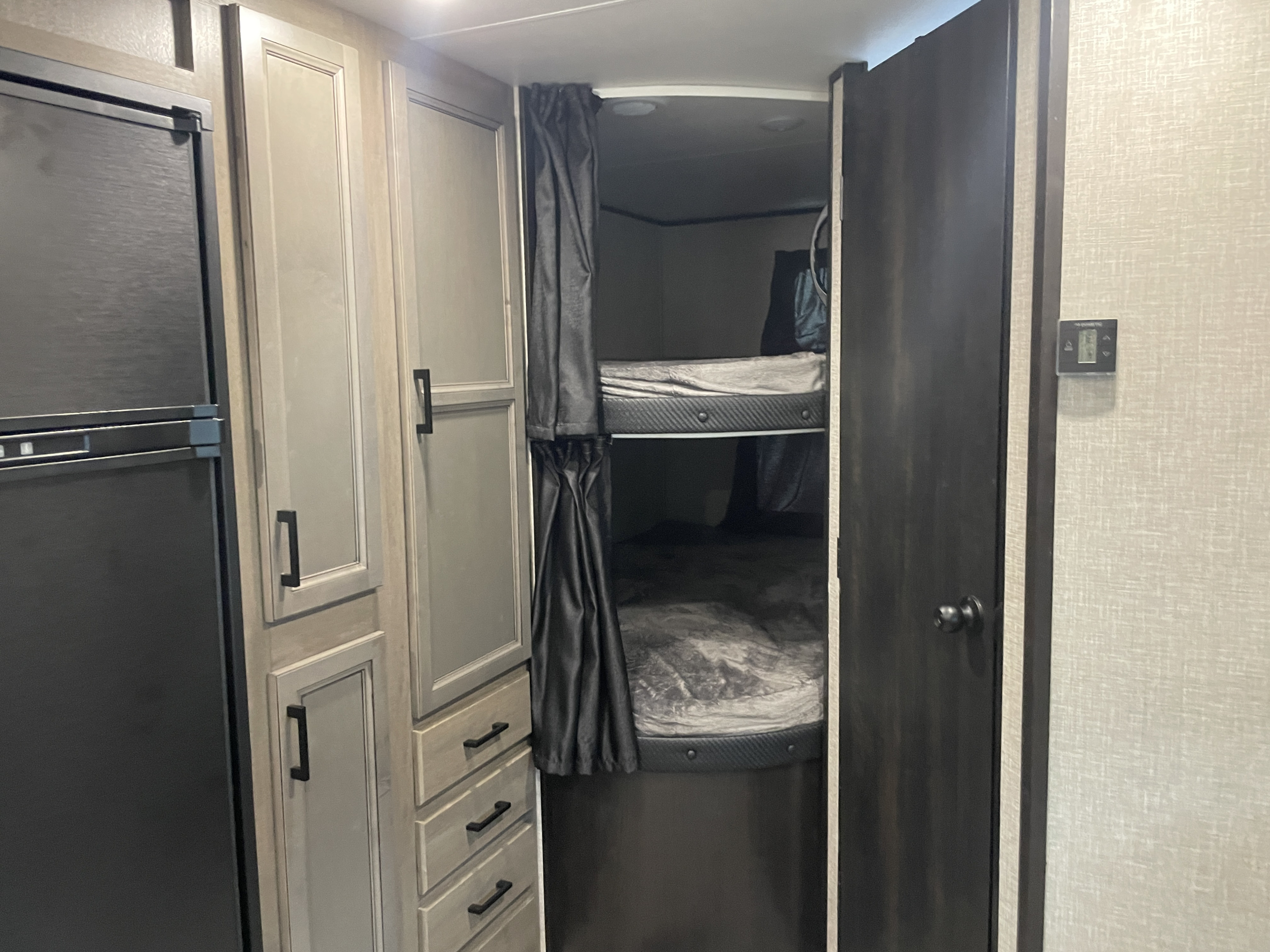 Cozy RV rental interior with black refrigerator, light wood cabinetry, and two bunk beds featuring privacy curtains & storage.. Jayco Jay Flight 2022