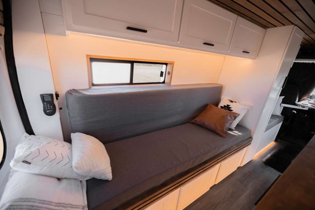 Cozy RV rental interior with grey bench seating, overhead cabinets, a small window, and a control panel on the wall.. Dodge 1500 2019