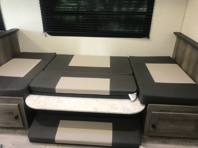 This RV rental features a dinette that converts into a bed, with grey and beige cushions, a table, and built-in storage.. KZ Sportsmen LE 2021