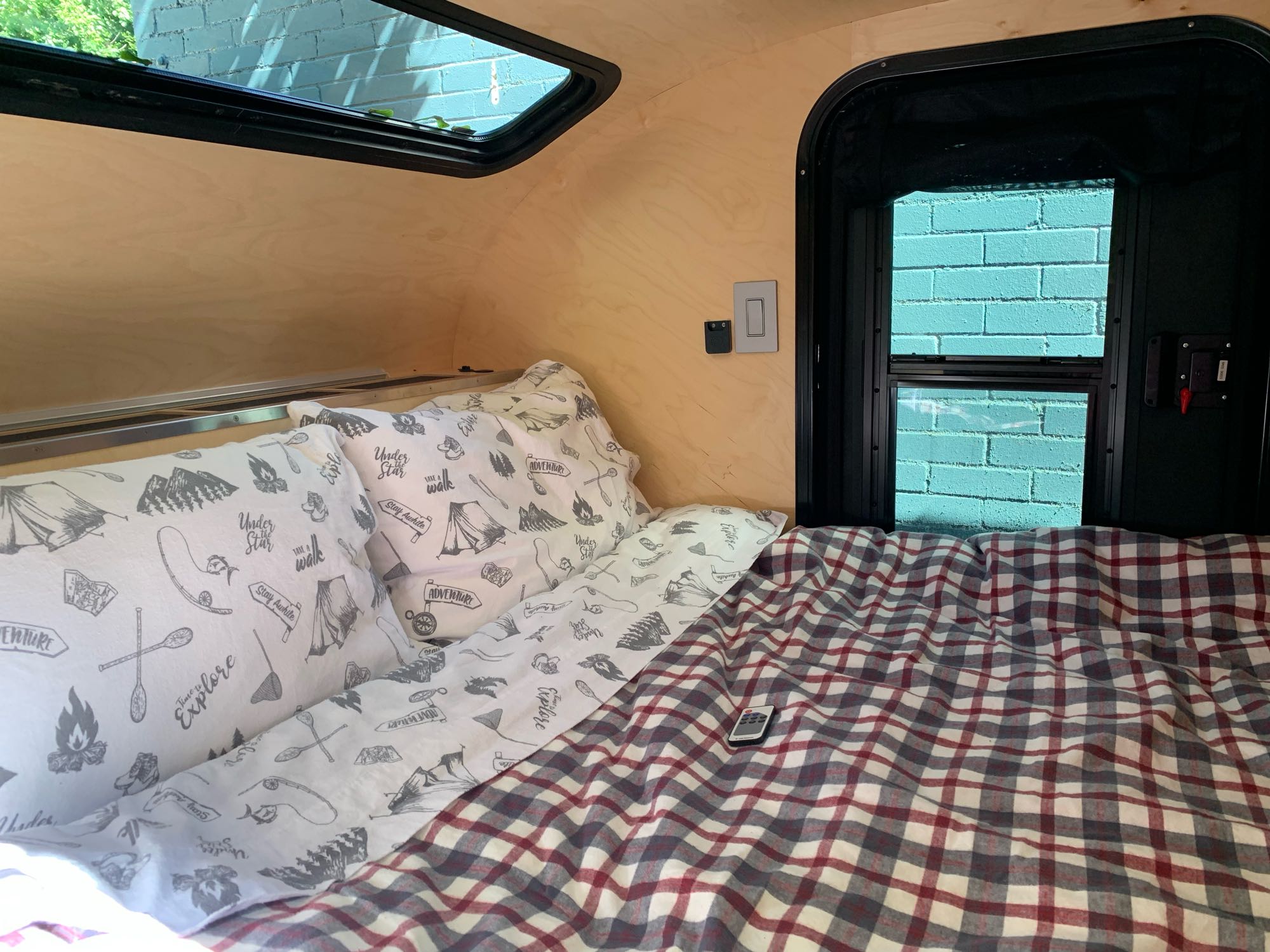 Cozy RV rental interior: wood-paneled bedroom with adventure-themed bedding, plaid comforter, and bright windows.. Escapod Topo Original 2022