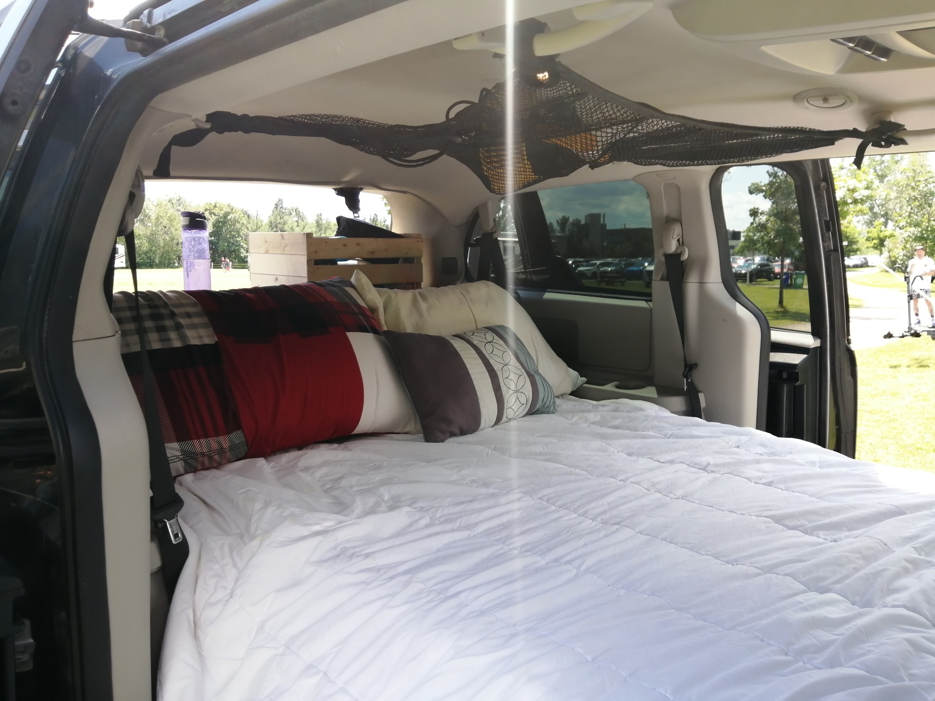 Cozy minivan interior features a bed with pillows & quilt for car camping. A practical RV rental alternative for travel adventures.. Dodge Grand Caravan 2016