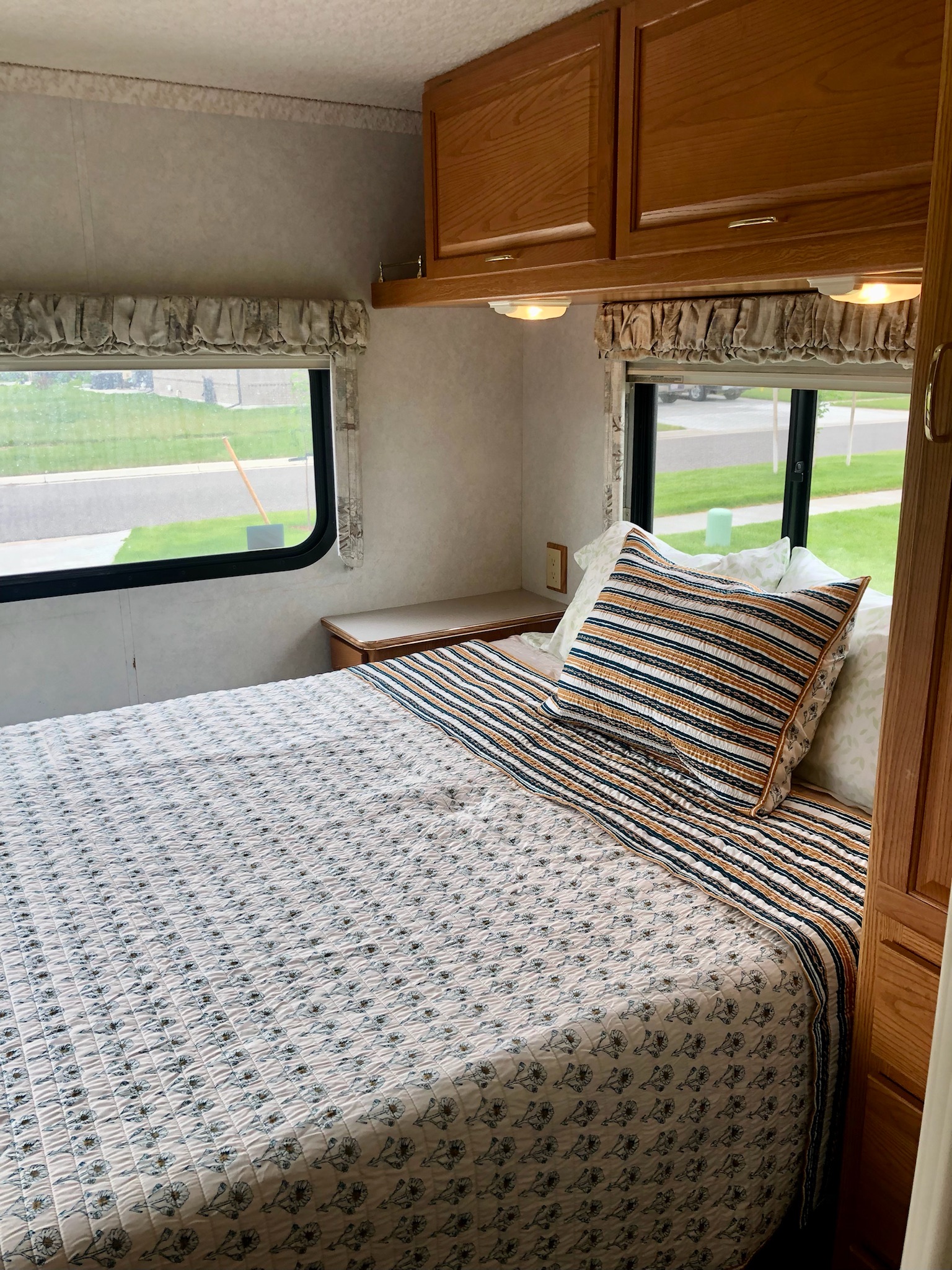 Spacious RV rental bedroom featuring a patterned bed, wood cabinets, and large windows for natural light and views.. Itasca Spirit 2001
