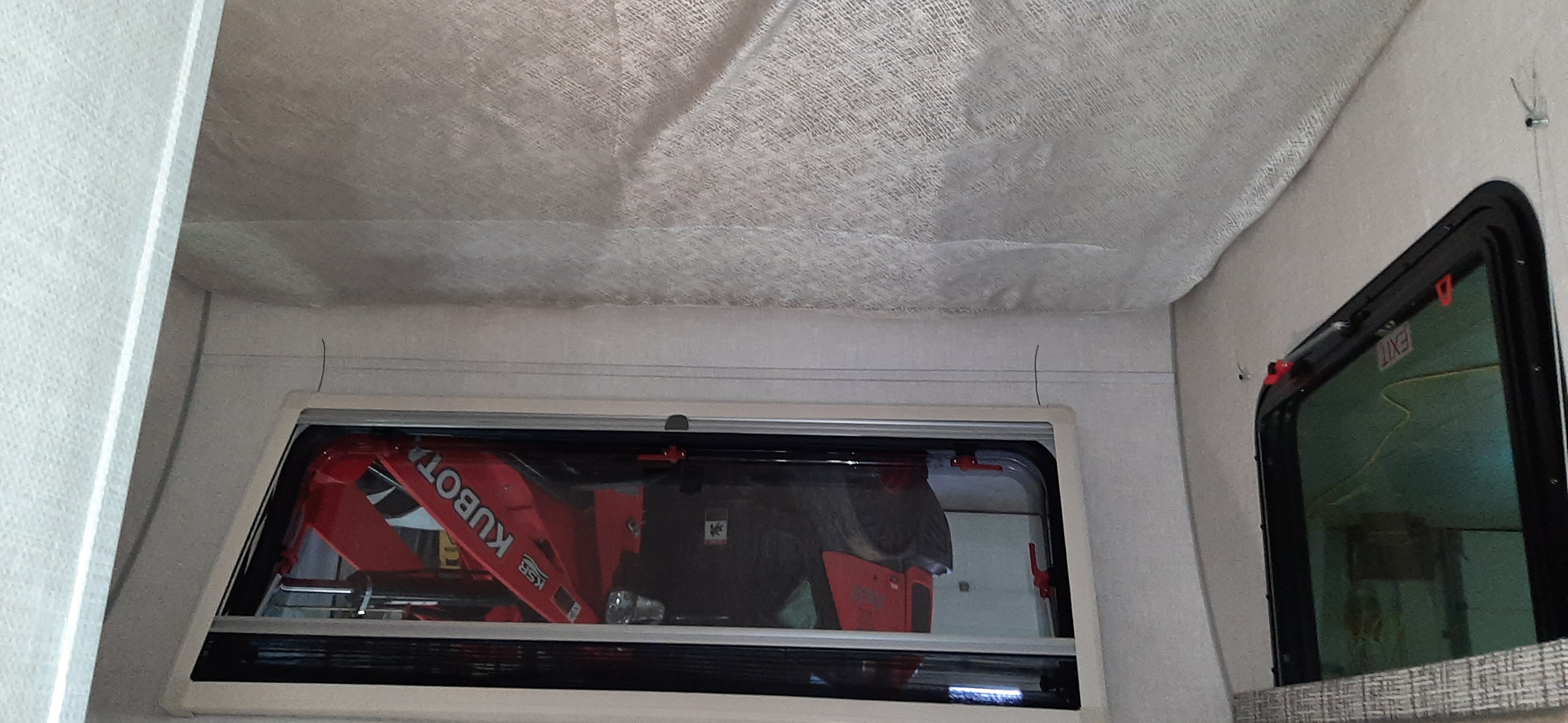 Inside an RV rental, a red Kubota excavator is seen through the window, with an "EXIT" sign visible on another window.. Forest River RPOD 190 2021