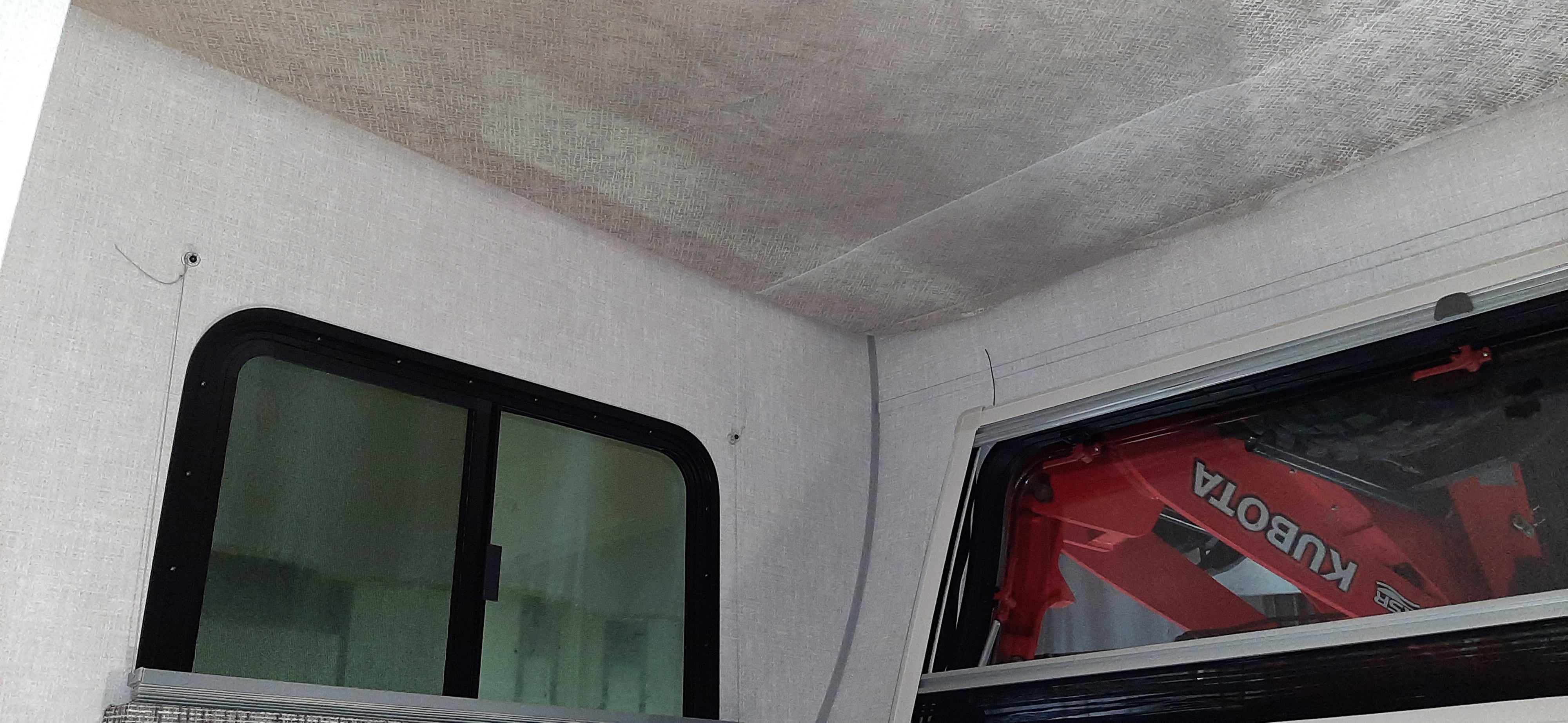 RV rental interior: two rounded windows, light textured walls/ceiling. A red Kubota is reflected, upside down, in one window.. Forest River RPOD 190 2021
