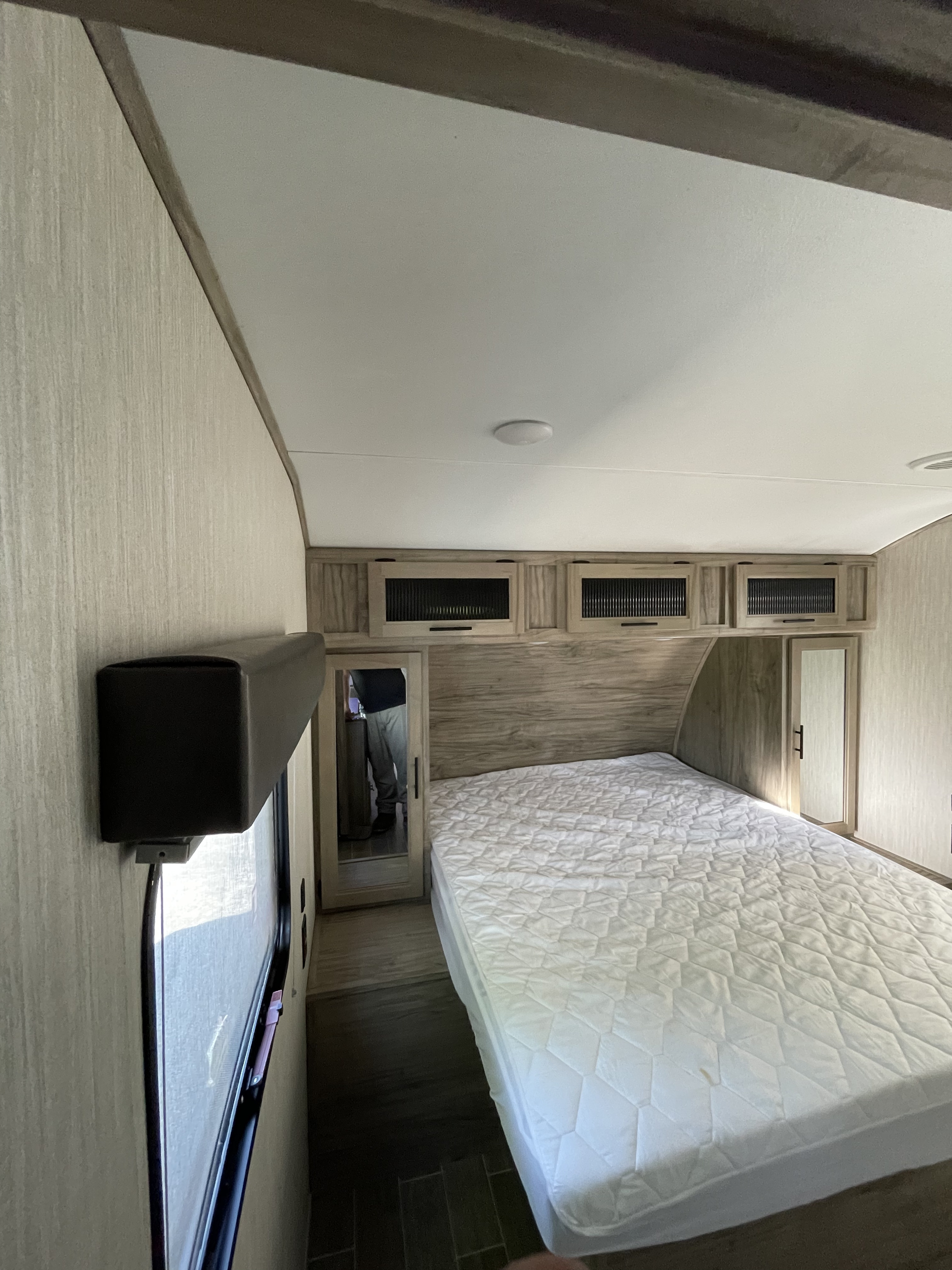 Inside an RV rental: a neat bedroom featuring a white quilted bed, wood-paneled walls, overhead cabinets, and mirrored closet doors.. Forest River Cherokee Alpha Wolf 2021