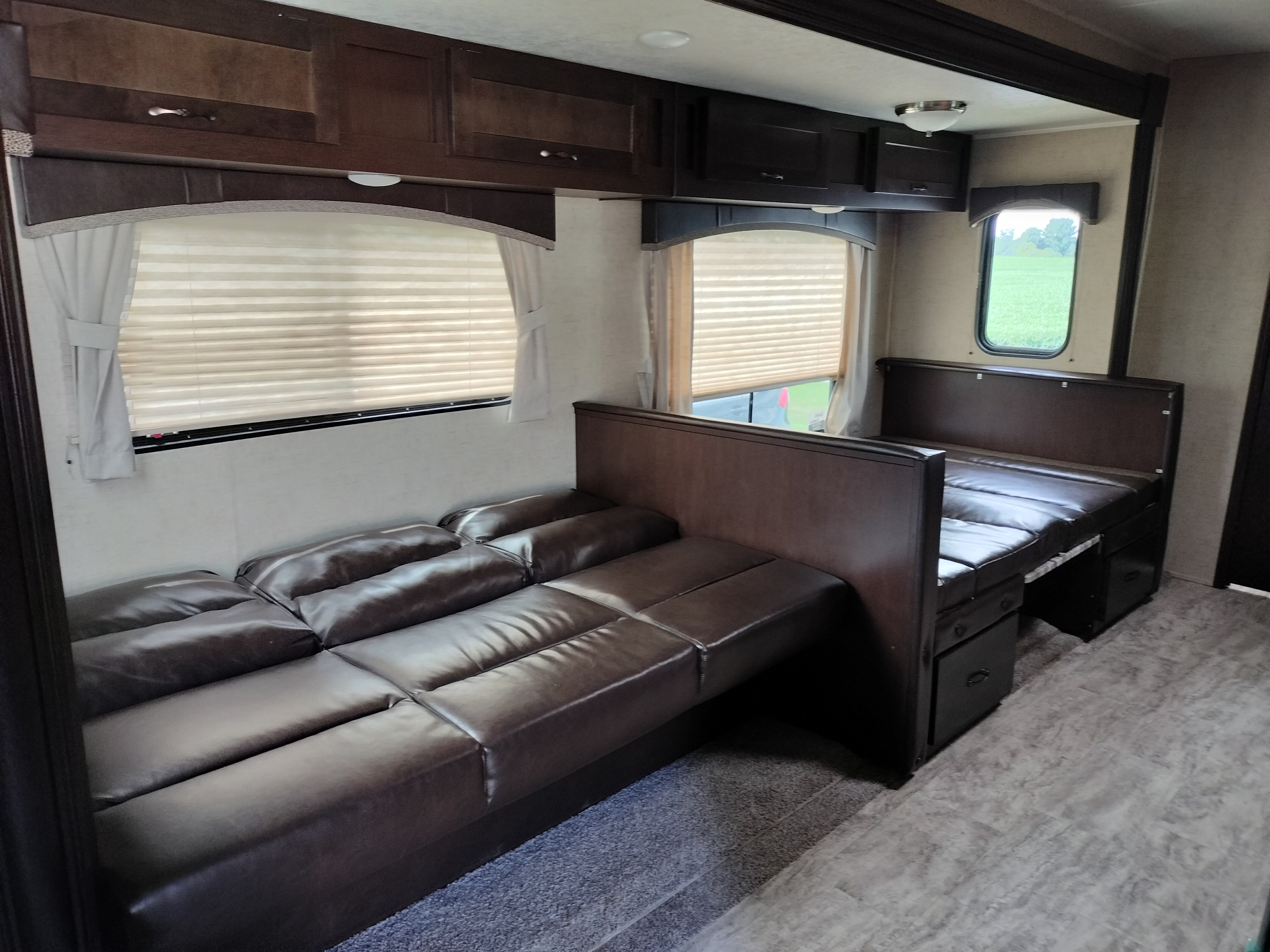 RV rental interior: Brown leatherette sofa/bed, dark wood cabinets, and windows with blinds in a modern camper.. East to West Della Terra 2020