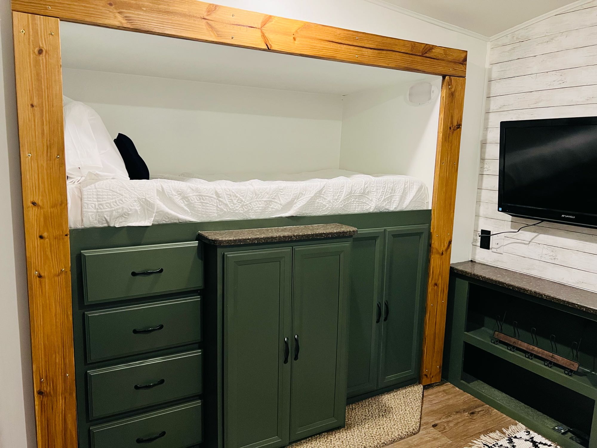 RV rental: Built-in bed with natural wood frame, white bedding, and ample dark green storage cabinets, ideal for compact travel.. Heartland RVs Greystone 2012