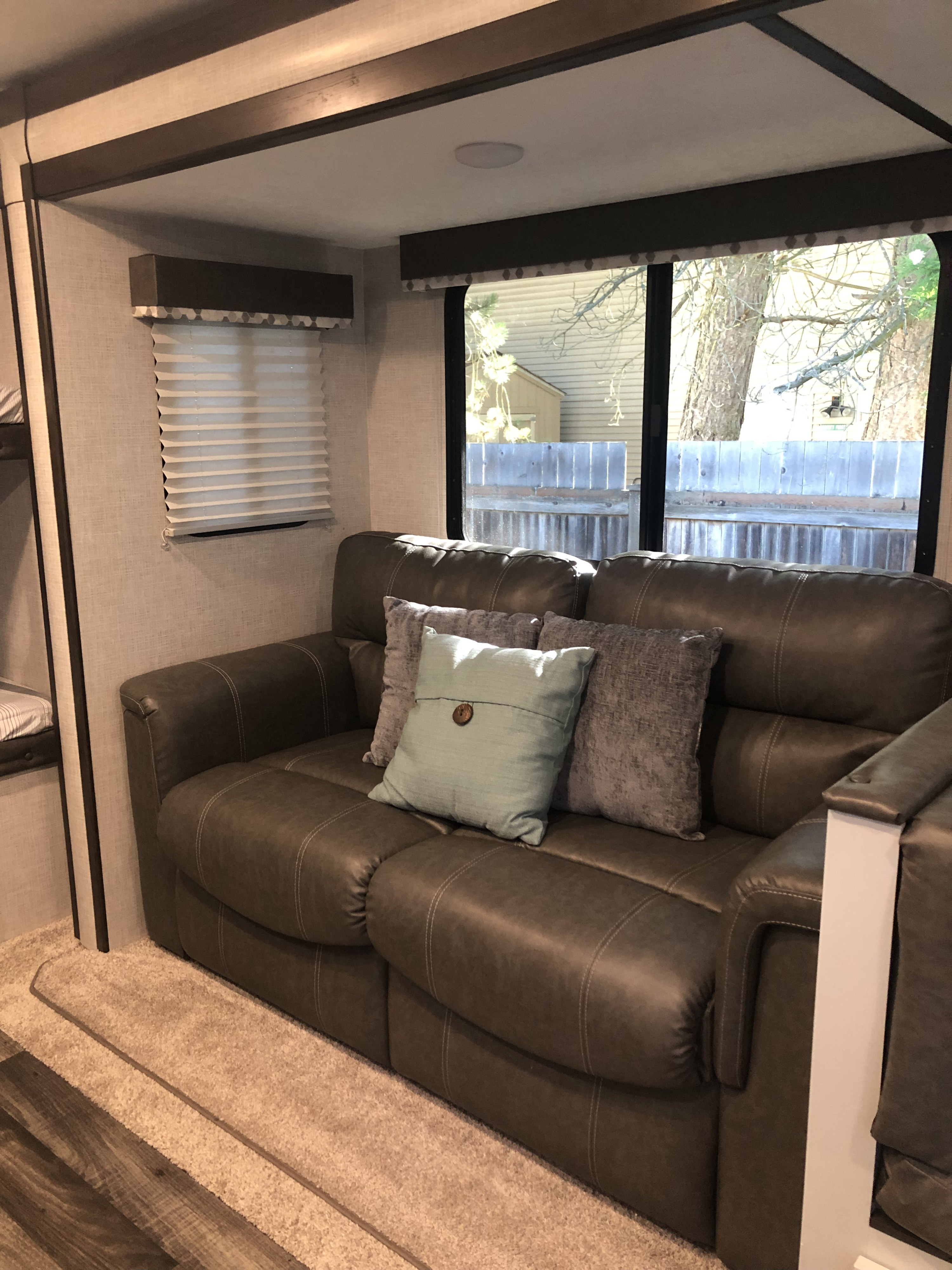 Inside this RV rental: a plush sofa with pillows, large window, pleated shades, and bunk area, creating a comfy living space.. Keystone RV Bullet Ultra Lite 2020