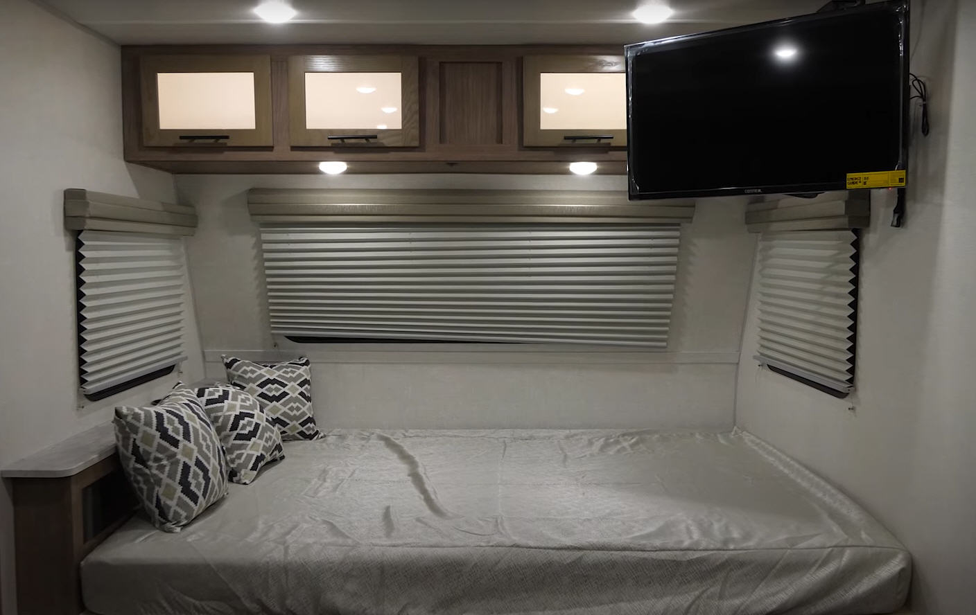 Cozy RV rental bedroom interior featuring a bed, patterned pillows, overhead cabinets, privacy blinds, and a mounted TV.. Forest River No Boundaries 19.8 2021