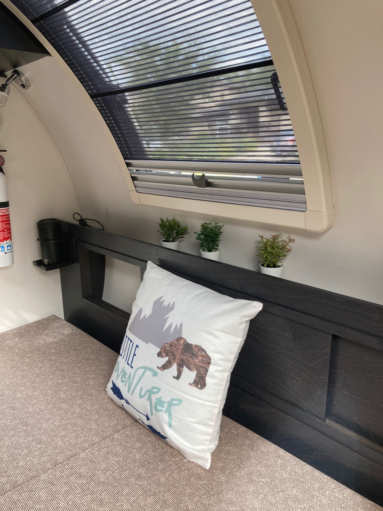 Inside a comfy rv rental: a bed with a bear pillow, plants, and a window with blinds, creating a cozy travel space.. Nucamp T@G 2022