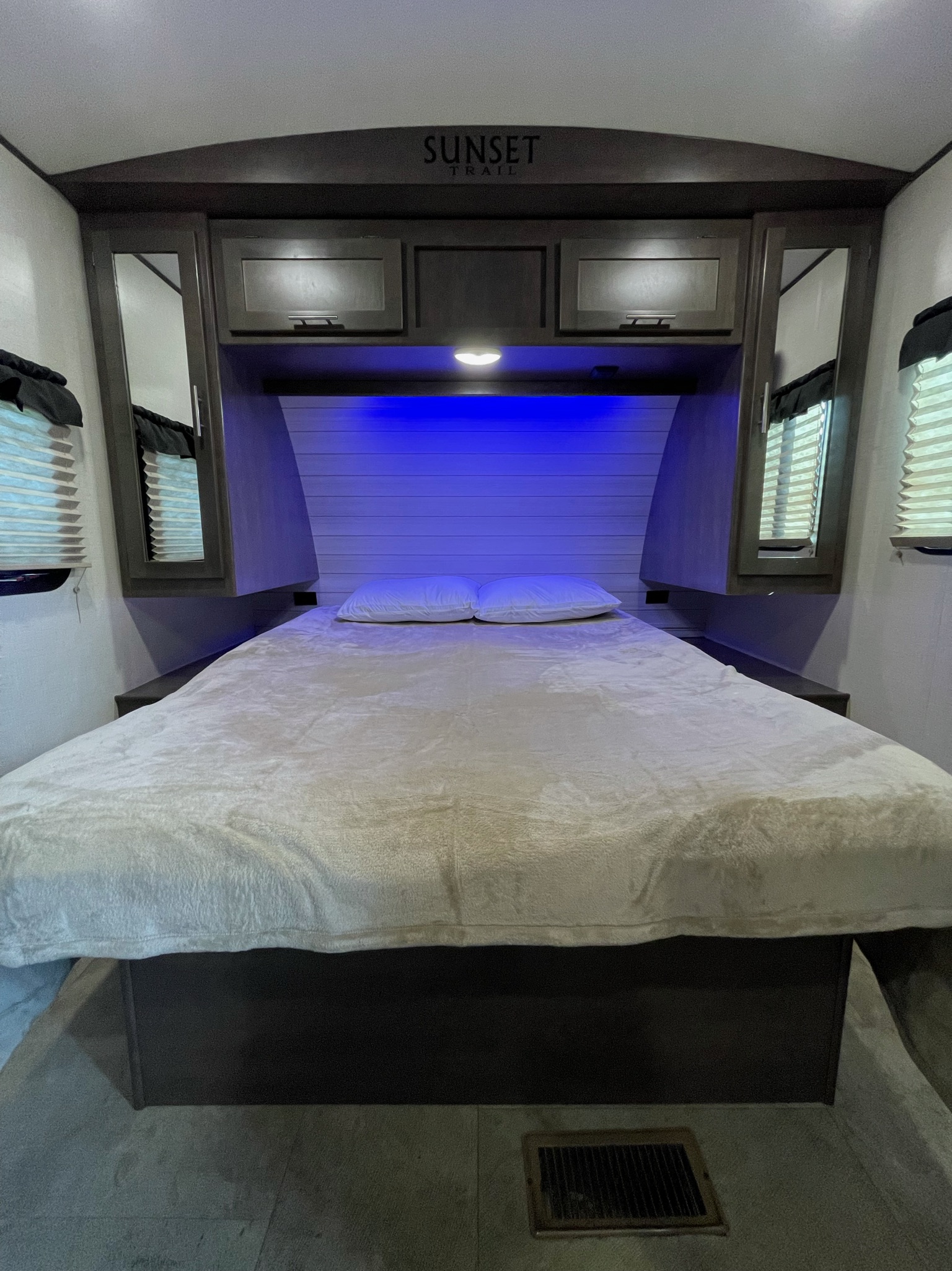 Keystone Sunset Trail RV rental bedroom with a comfortable bed, blue light, overhead storage, and side windows.. Crossroads RV Sunset Trail Super Lite 2019