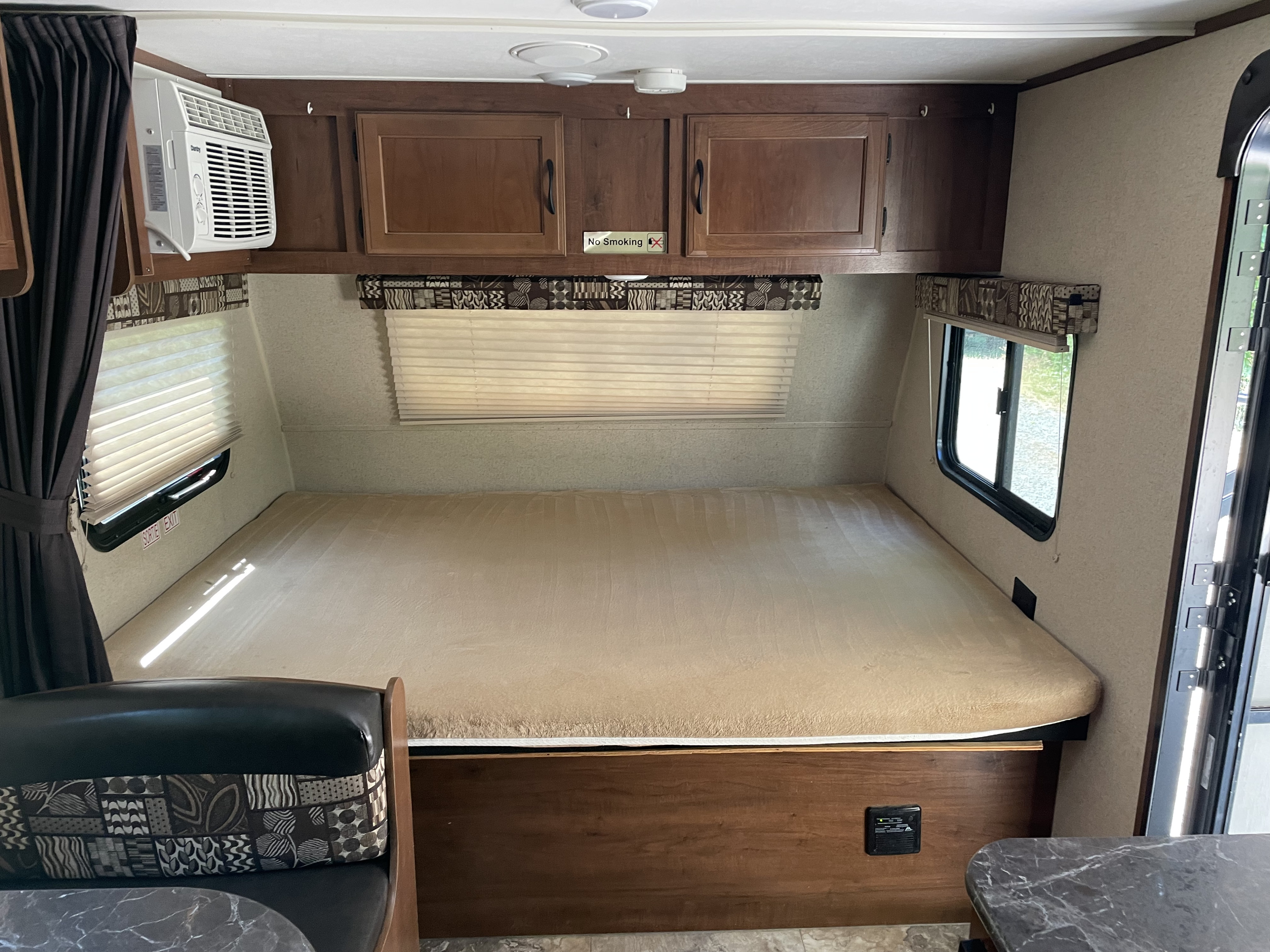 A clear view of an RV rental bedroom, showing a large bed, wooden cabinets, and a wall-mounted AC unit.. Jayco Jay Flight SLX 2016
