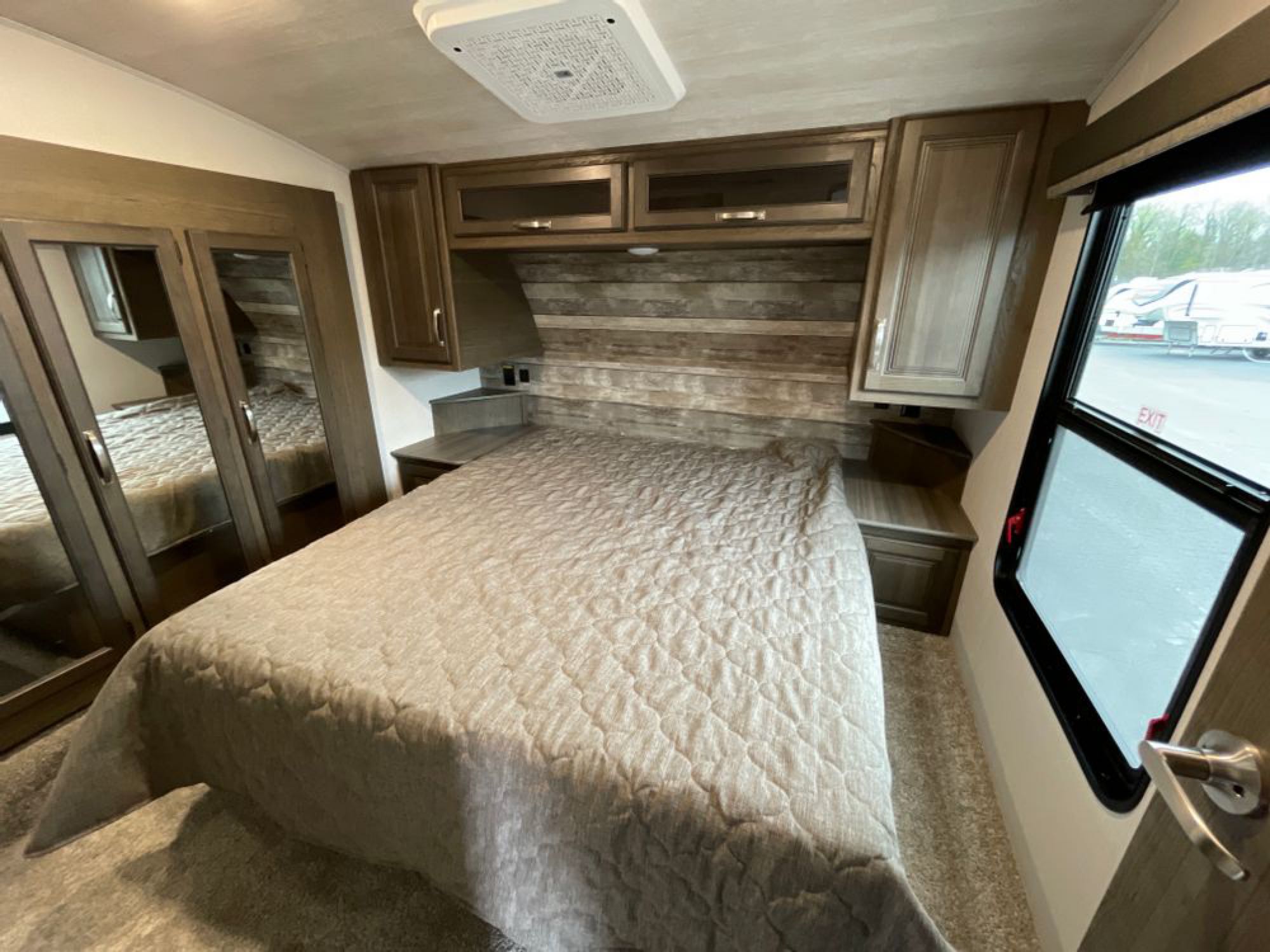 This RV rental bedroom features a large, comfortable bed, mirrored closet, and ample overhead cabinets. Perfect for mobile living.. Keystone RV Cougar 32BHS 2021