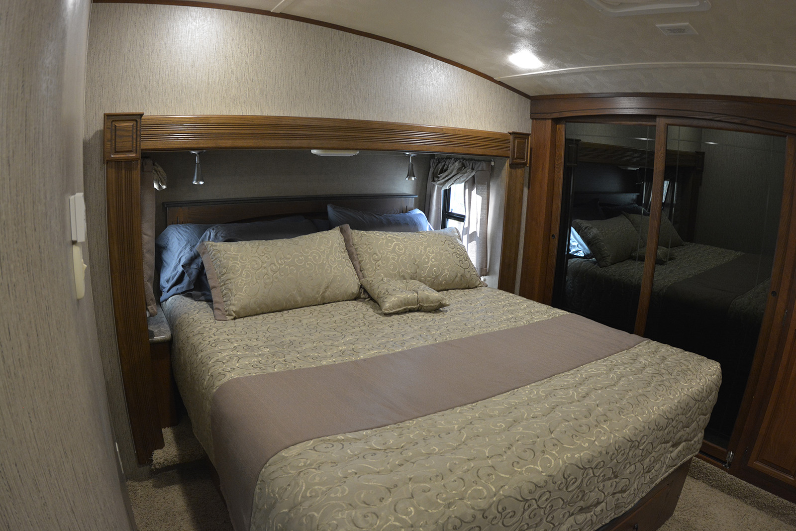 Relax in this RV rental's cozy bedroom. It features a made bed, built-in lighting, and mirrored closet doors for travel comfort.. Forest River Palomino Sabre 2015