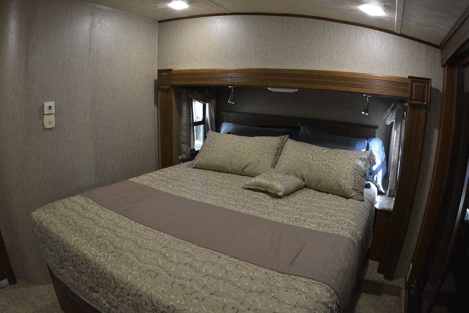 Inside a comfortable RV rental bedroom, showing a large bed with patterned bedding, a wooden headboard, and ambient lighting.. Forest River Palomino Sabre 2015