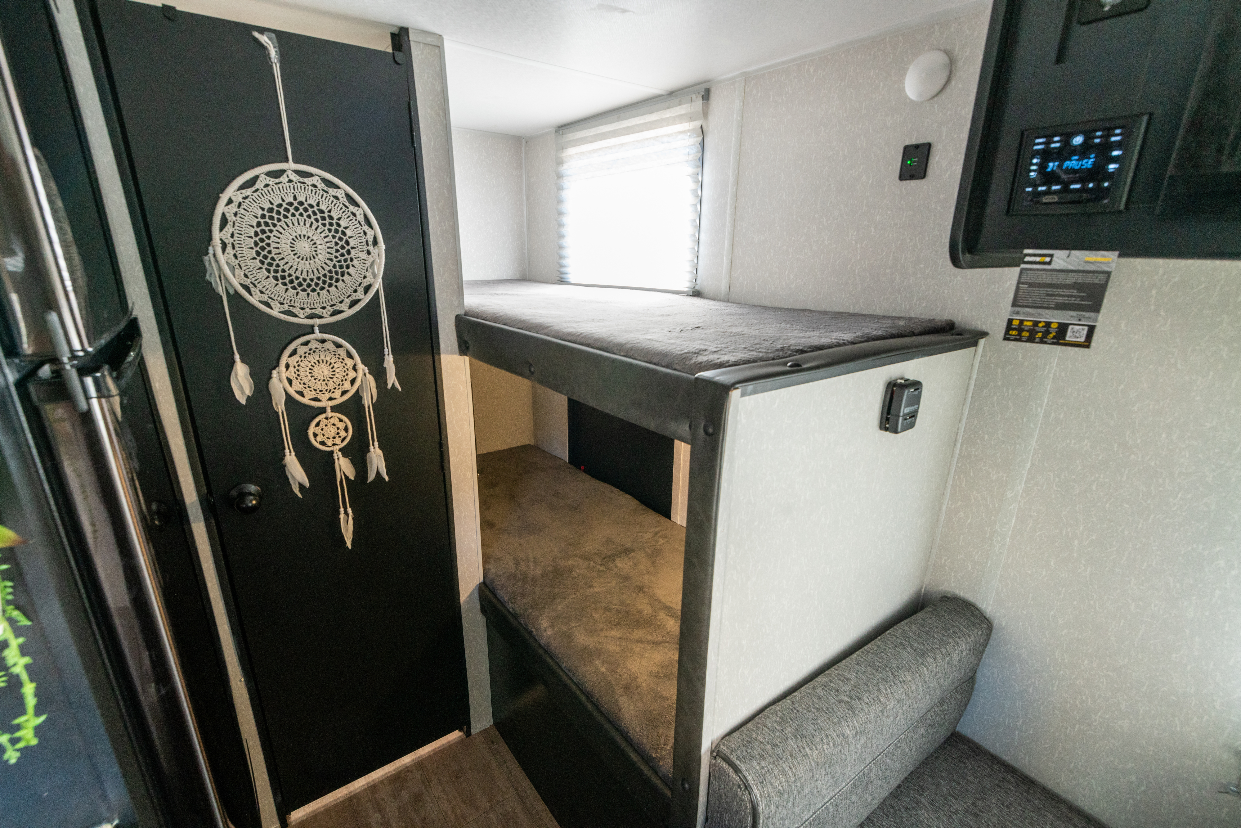 Cozy RV rental bunk area: features comfy grey beds, a sofa, a white dream catcher on a black door, and essential controls.. Forest River Cherokee Wolf Pup 2022