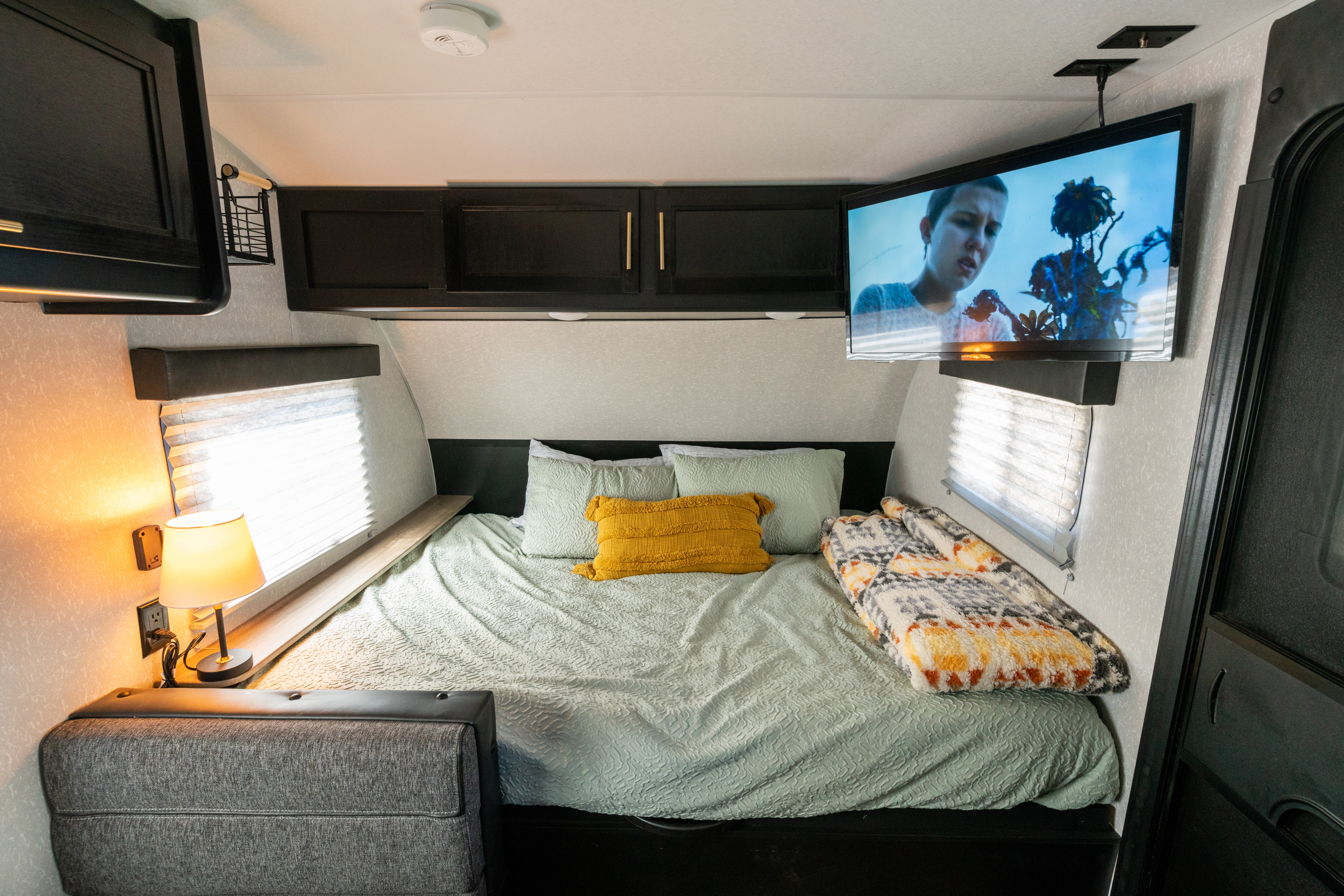 Cozy RV rental bedroom with a bed, mounted TV, overhead cabinets, and a bedside lamp, perfect for unwinding.. Forest River Cherokee Wolf Pup 2022