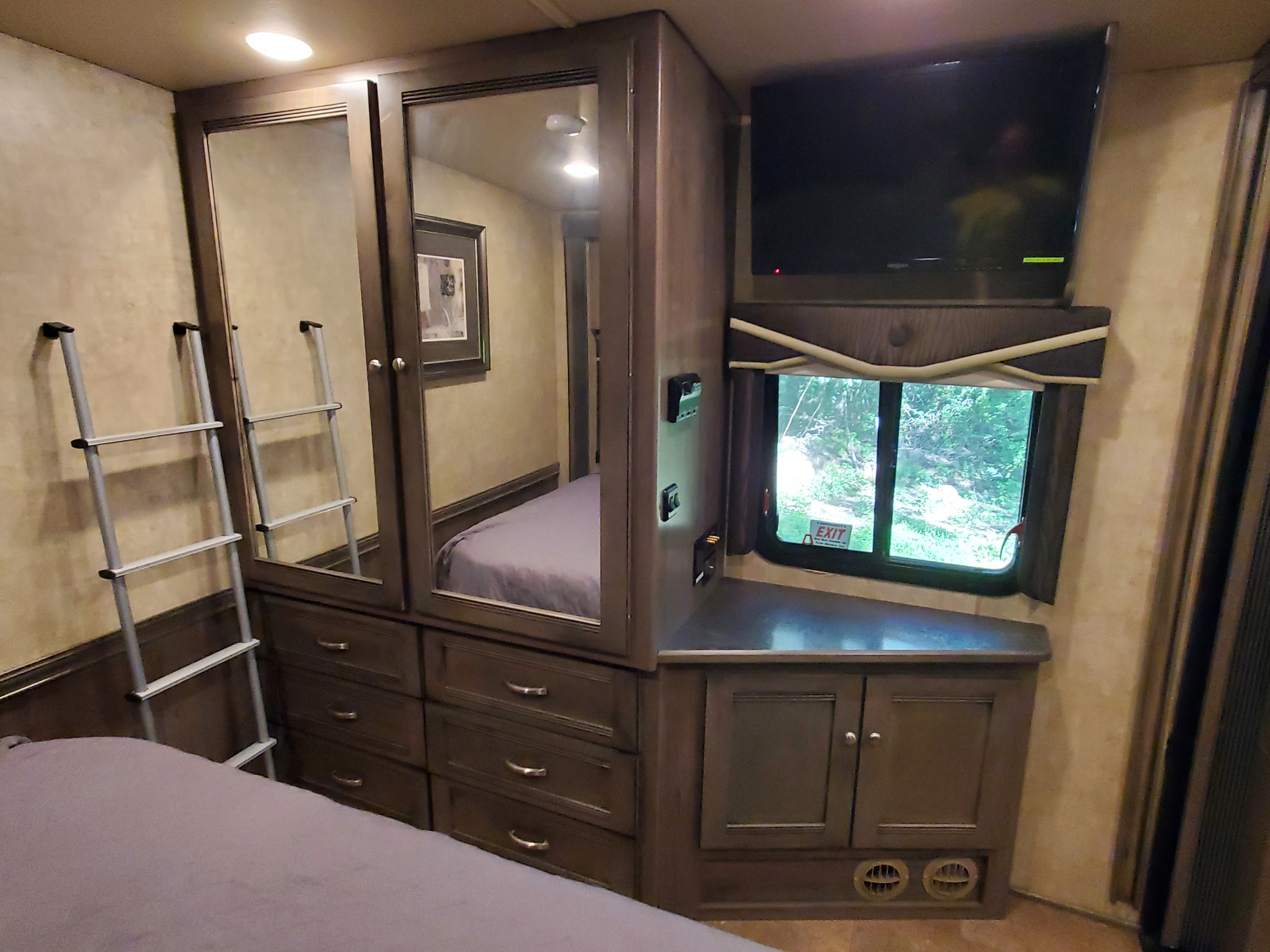 Inside an RV rental bedroom: large mirrored wardrobe, bed, mounted TV, window with view, and a ladder for bunk access.. Itasca Sunova 2016