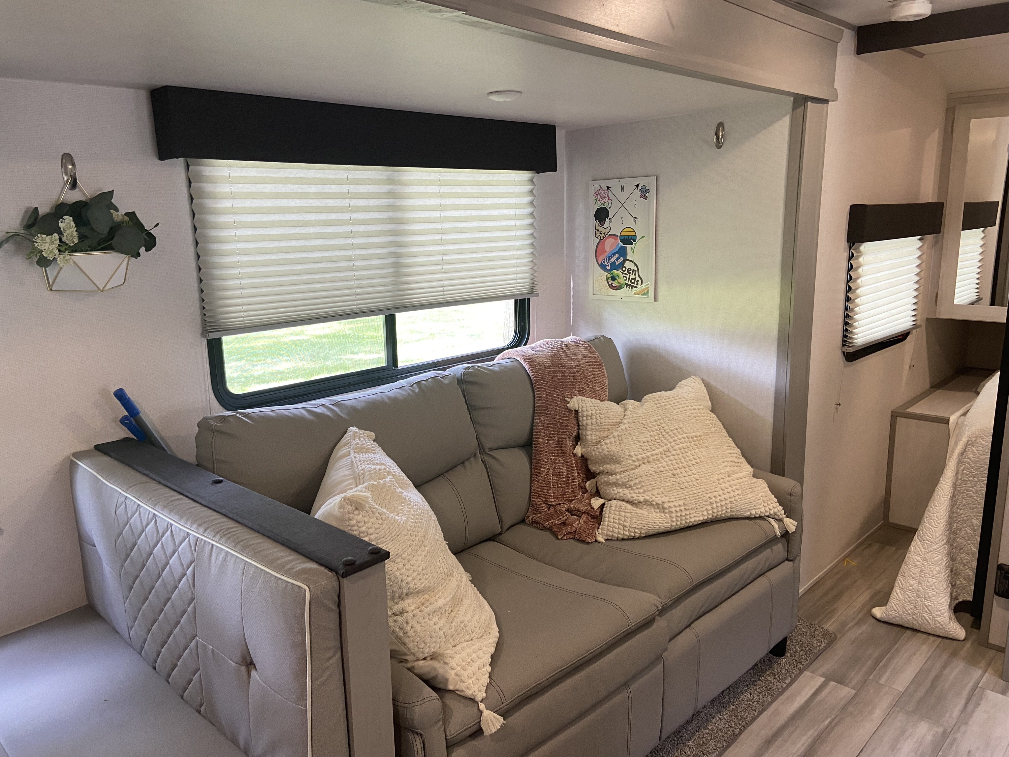 Inviting RV rental interior: grey couch with soft pillows, throw, and window view, creating a comfortable living area.. Forest River Tracer LE 2022