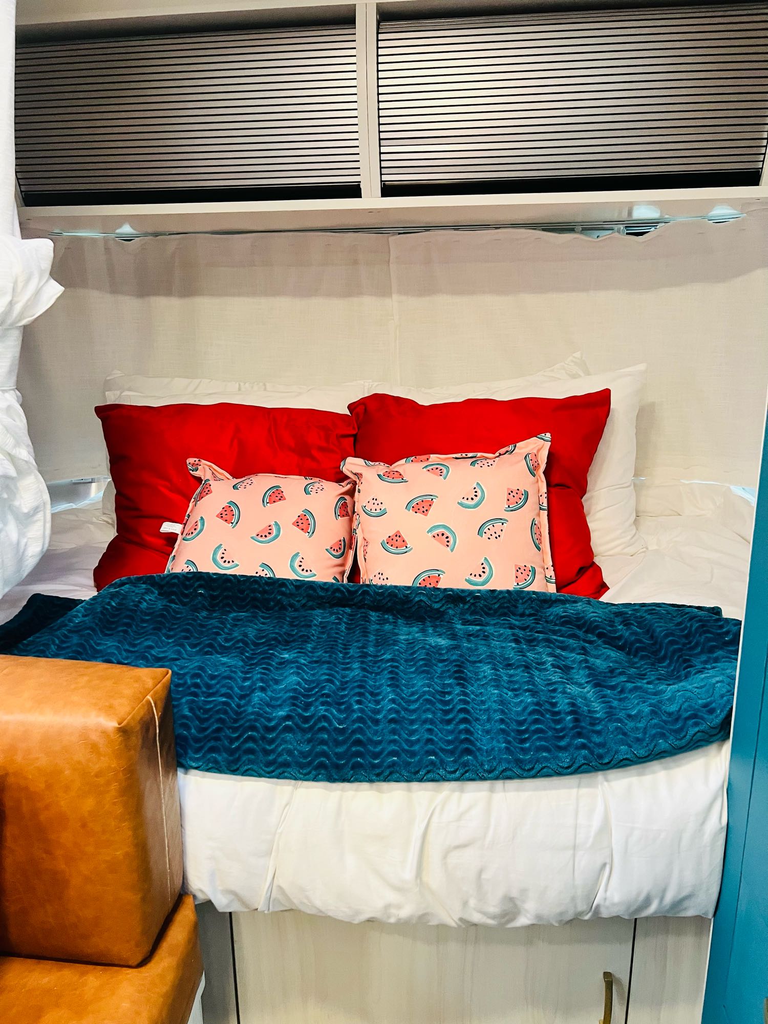 Cozy RV rental bedroom with red & watermelon pillows, teal blanket, and white sheets. Comfy sleeping space.. Airstream Bambi 2022