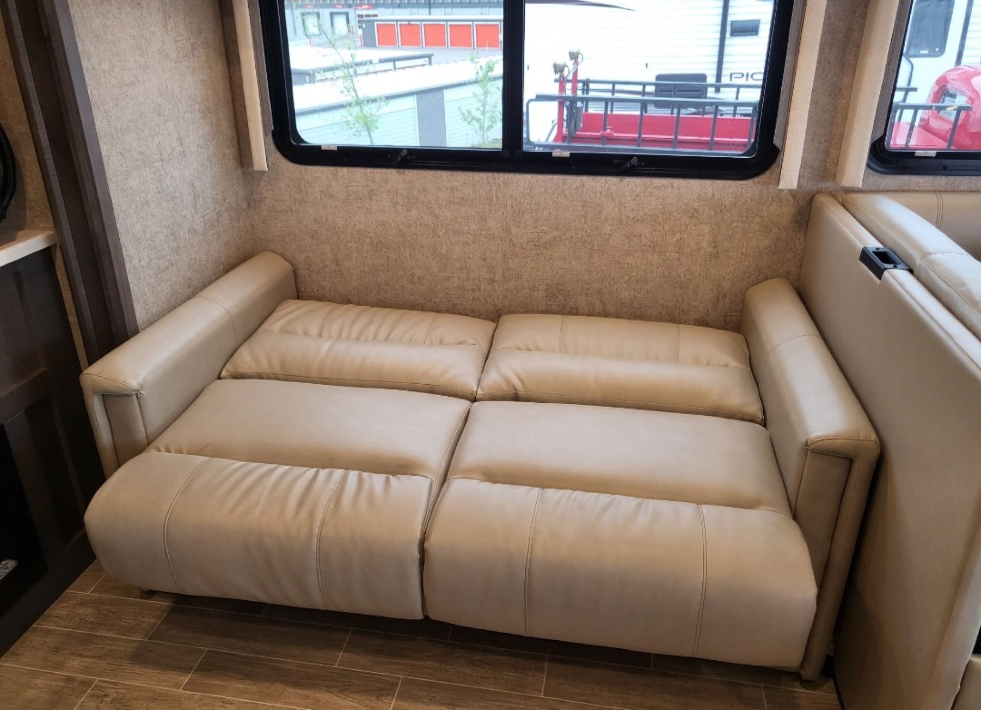 Cream multi-section sofa, appearing as a bed, in an RV rental. Spacious interior with windows and wood-look flooring.. Thor Miramar 2022