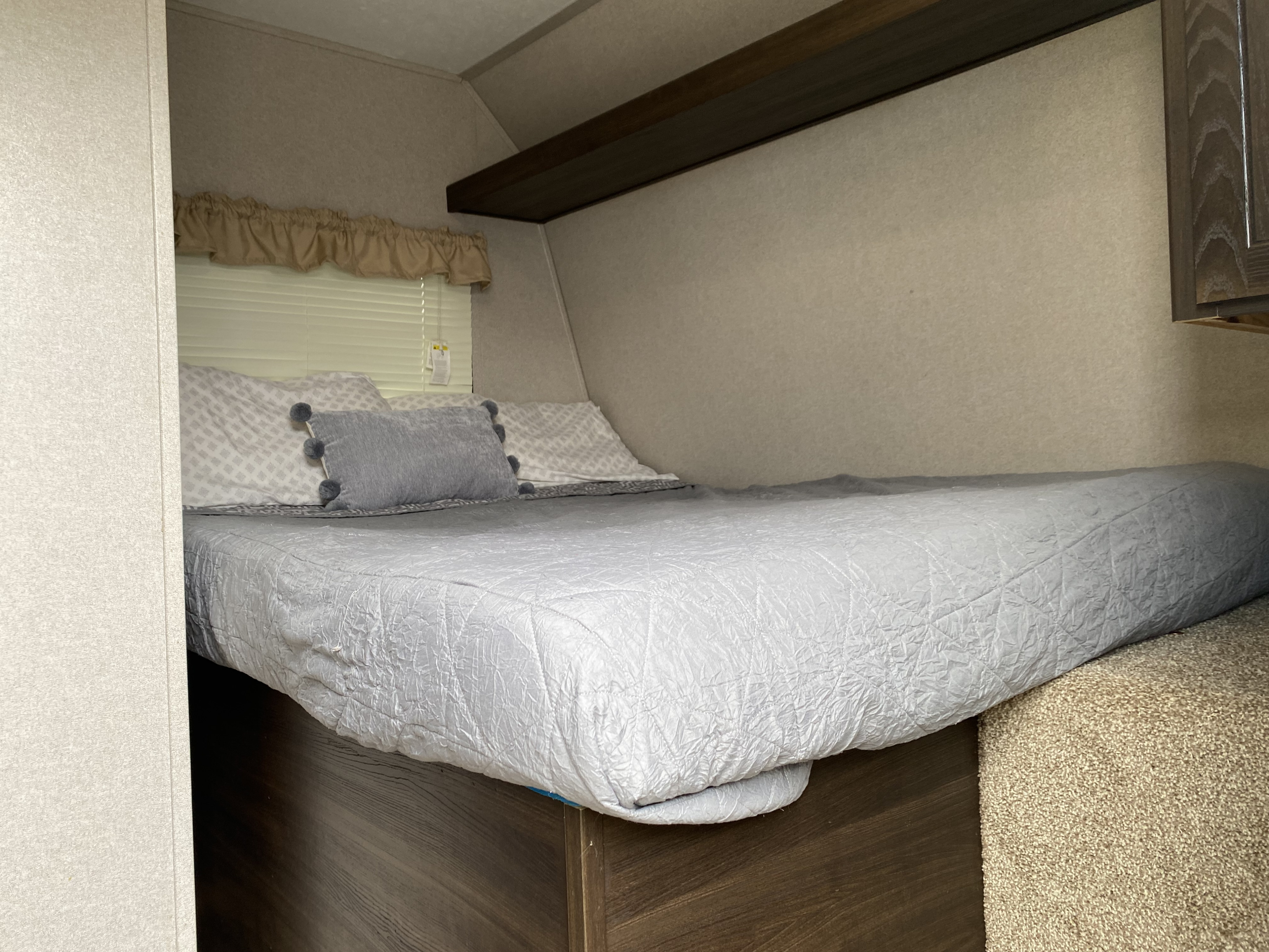 Inside an RV rental: A neat bed with grey comforter and pillows, a window with blinds, and built-in shelving.. Keystone RV Springdale 2019