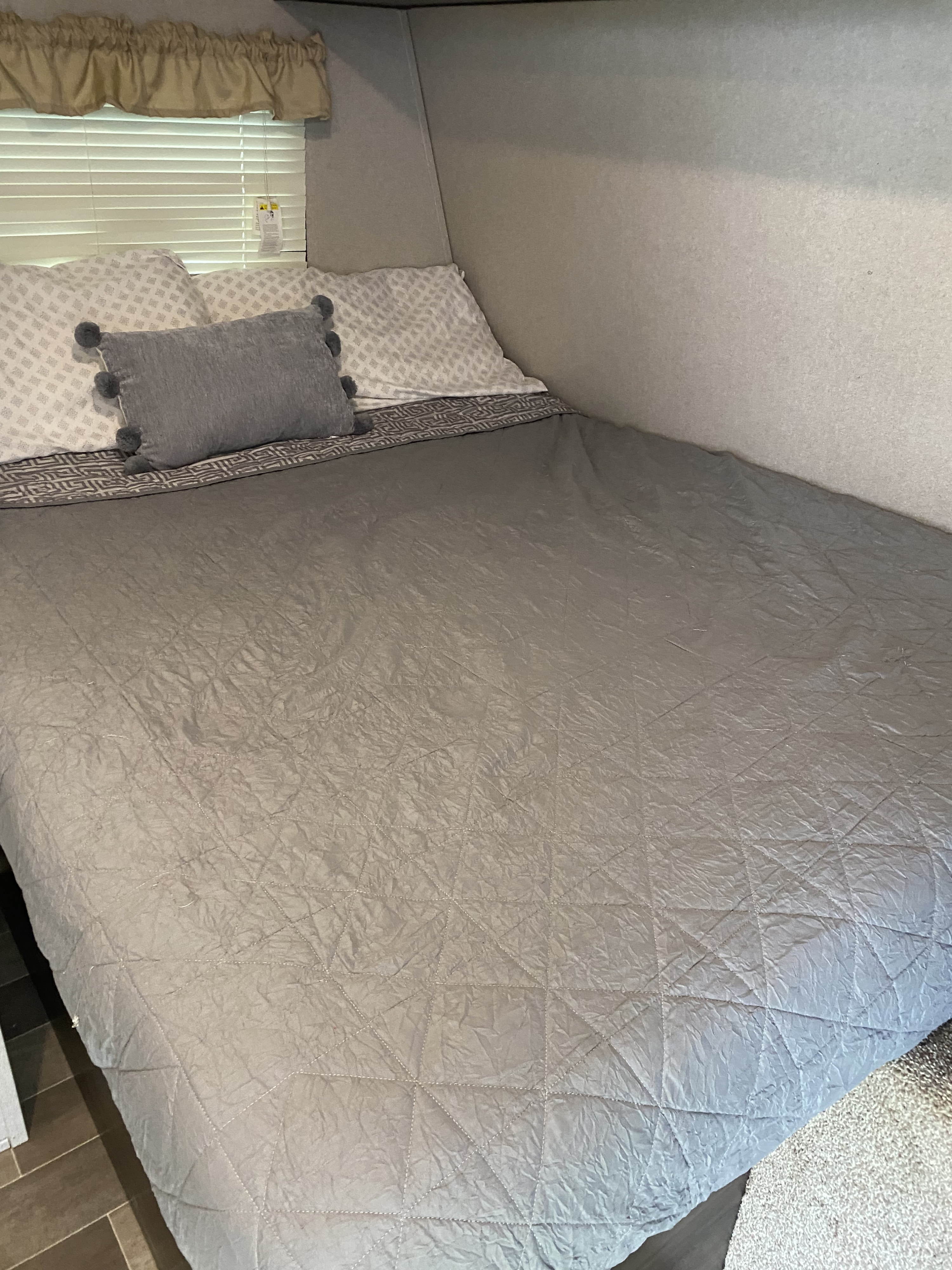 Relax in this comfortable RV rental bedroom, featuring a neatly made bed with grey quilt & patterned pillows.. Keystone RV Springdale 2019