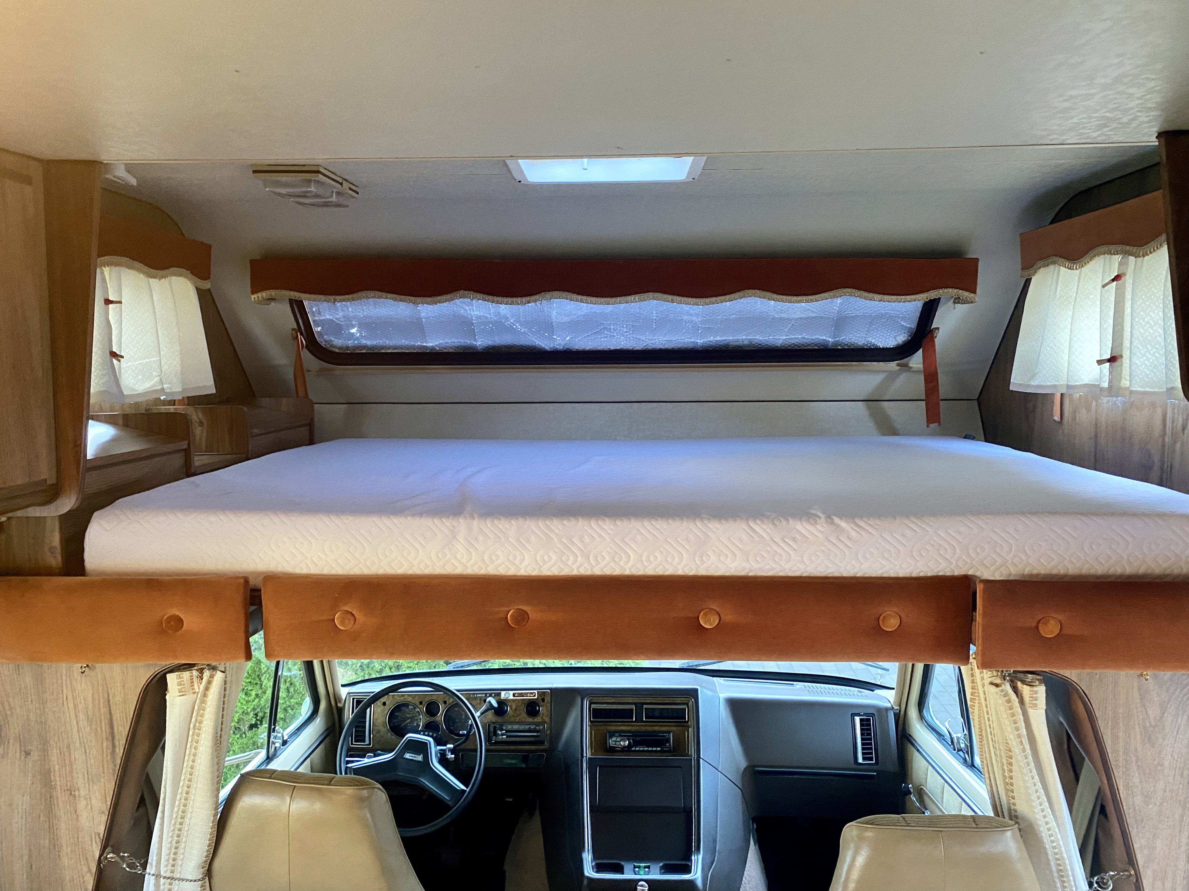 Spacious RV rental interior featuring a comfortable cabover bunk bed and a classic dashboard.. Gmc Motorhome 1985