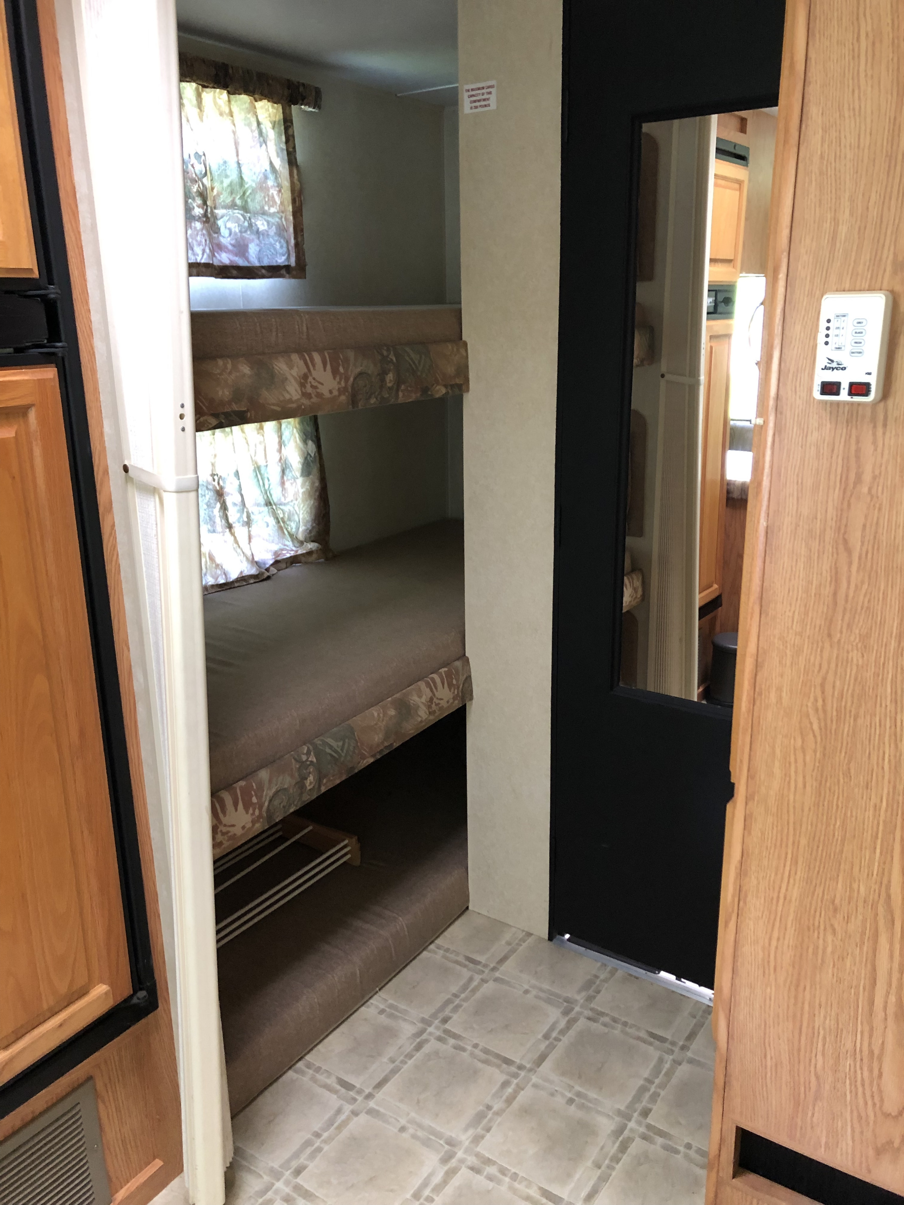 Cozy RV rental interior showcasing two bunk beds, a window with curtains, and tile flooring. Ideal for family trips.. Jayco Eagle 2003