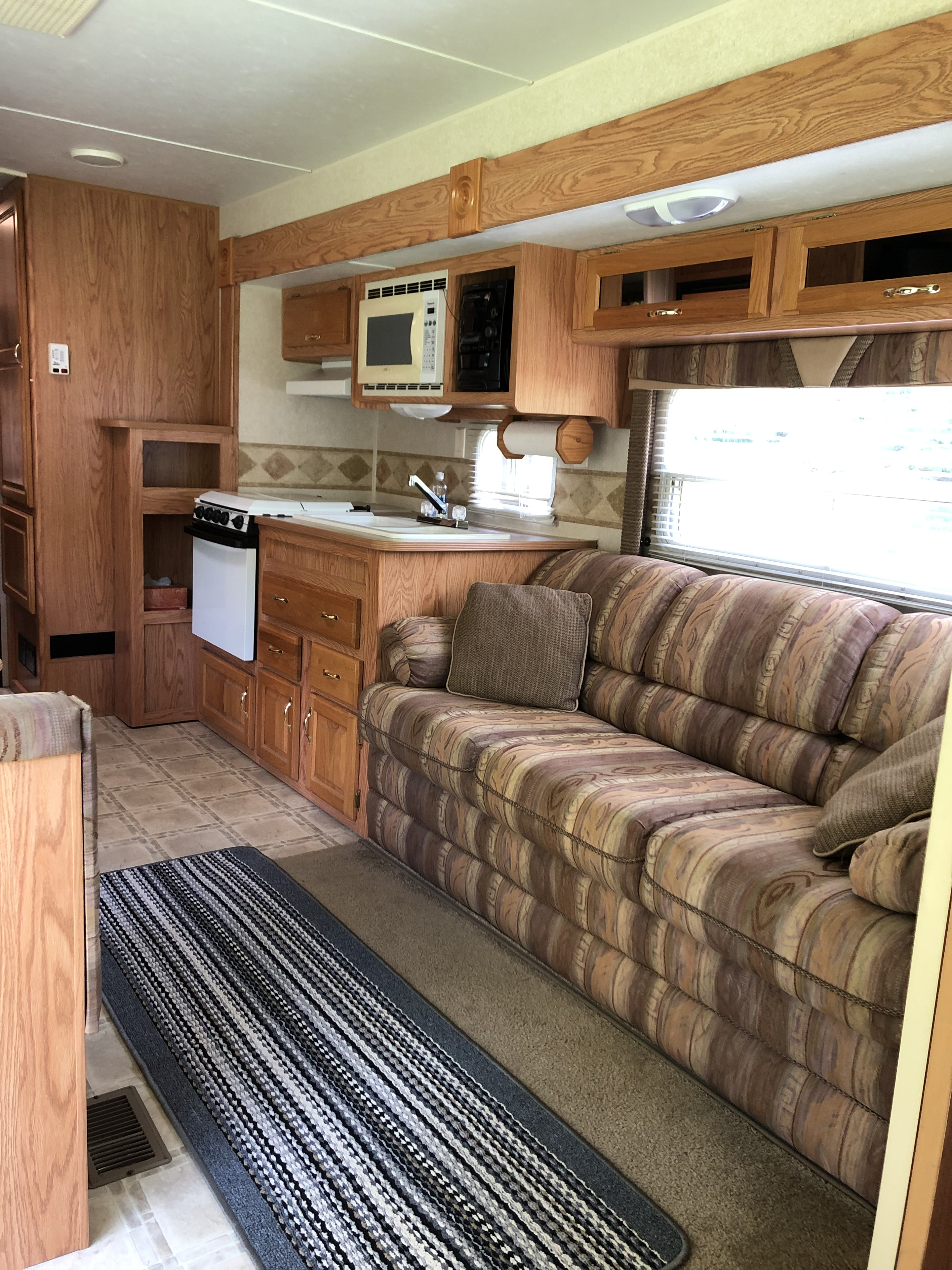 RV rental interior showcasing a kitchen with microwave/stove, patterned sofa, wood cabinets, and mixed flooring.. Jayco Eagle 2003